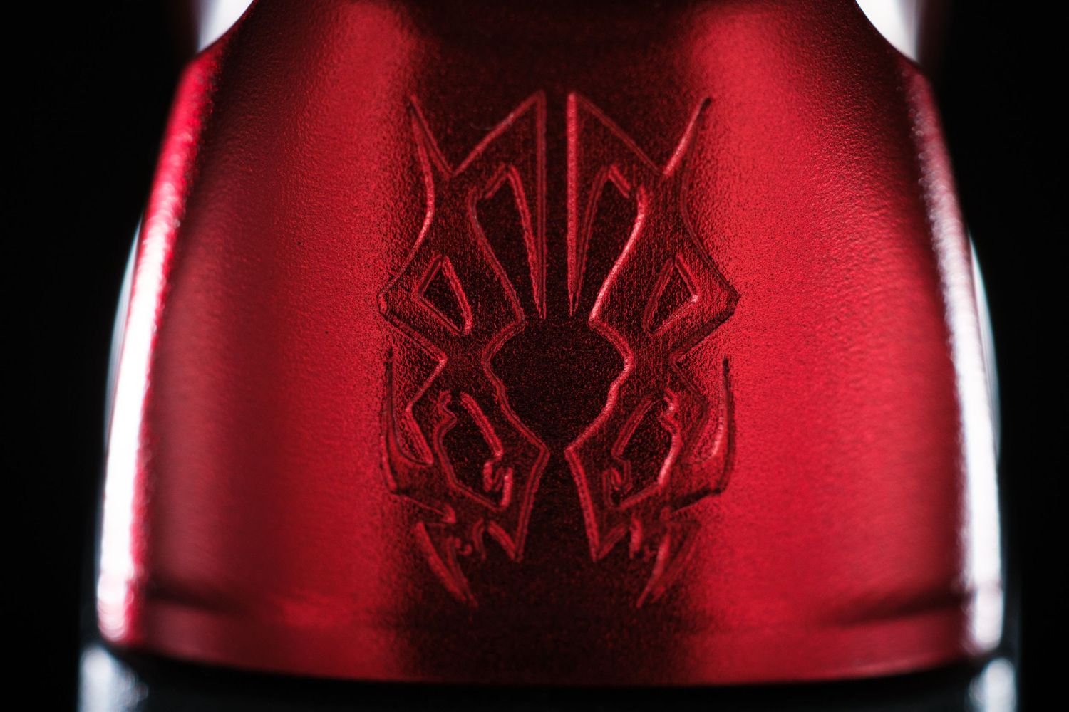 Close-up of red bottle with embossed tribal design pattern against dark background.