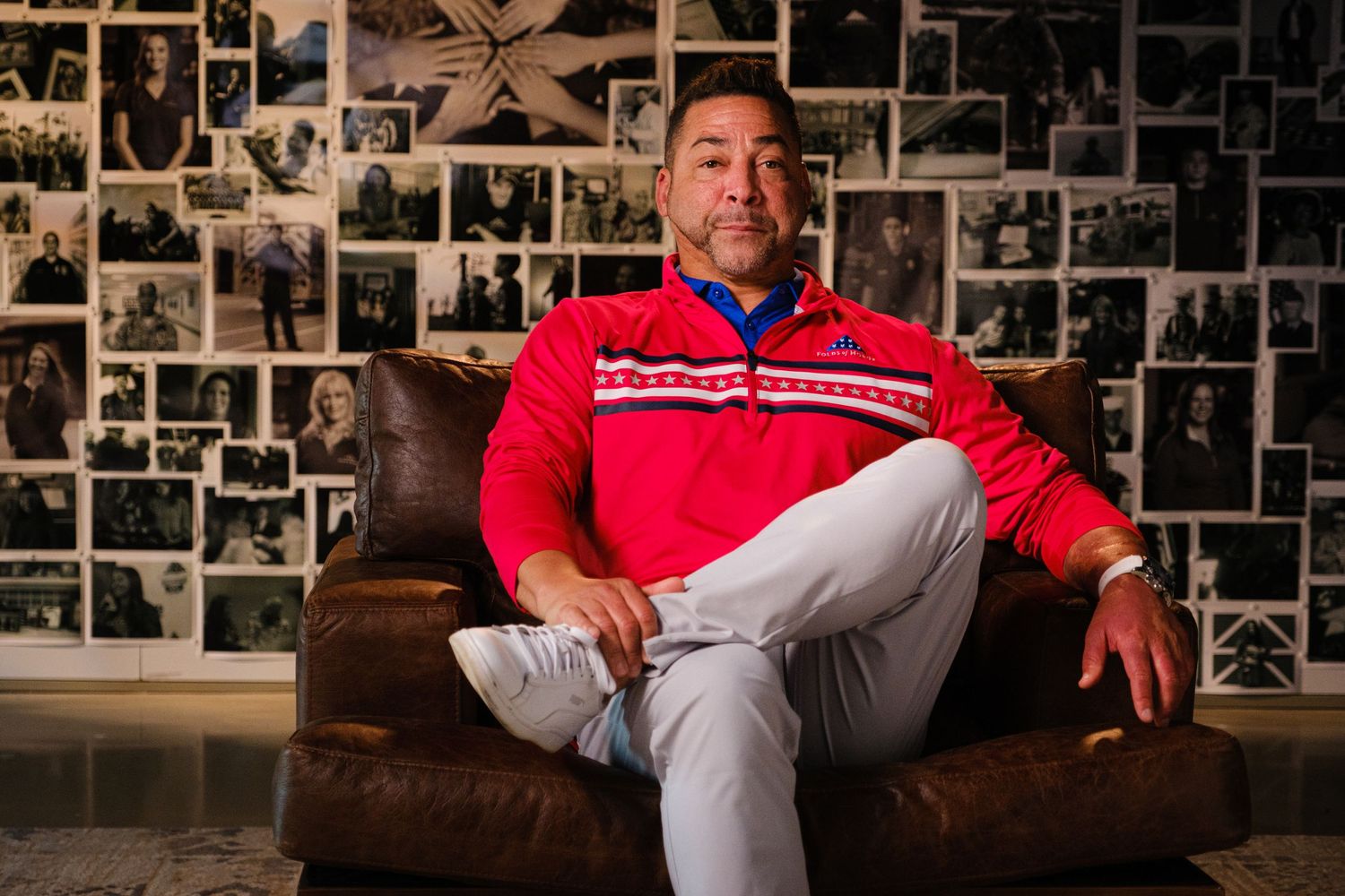 Person in red sweater seated on leather couch against wall covered in black and white photos.