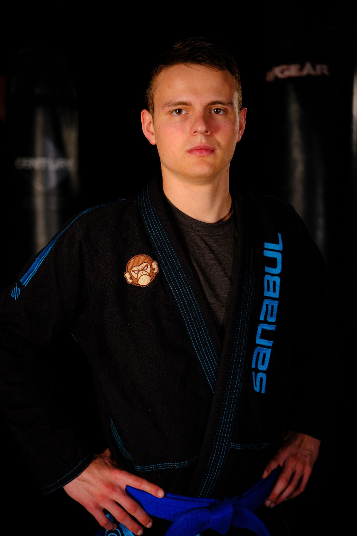 Martial artist wearing a black and blue Sanabul gi poses in a dark studio setting.