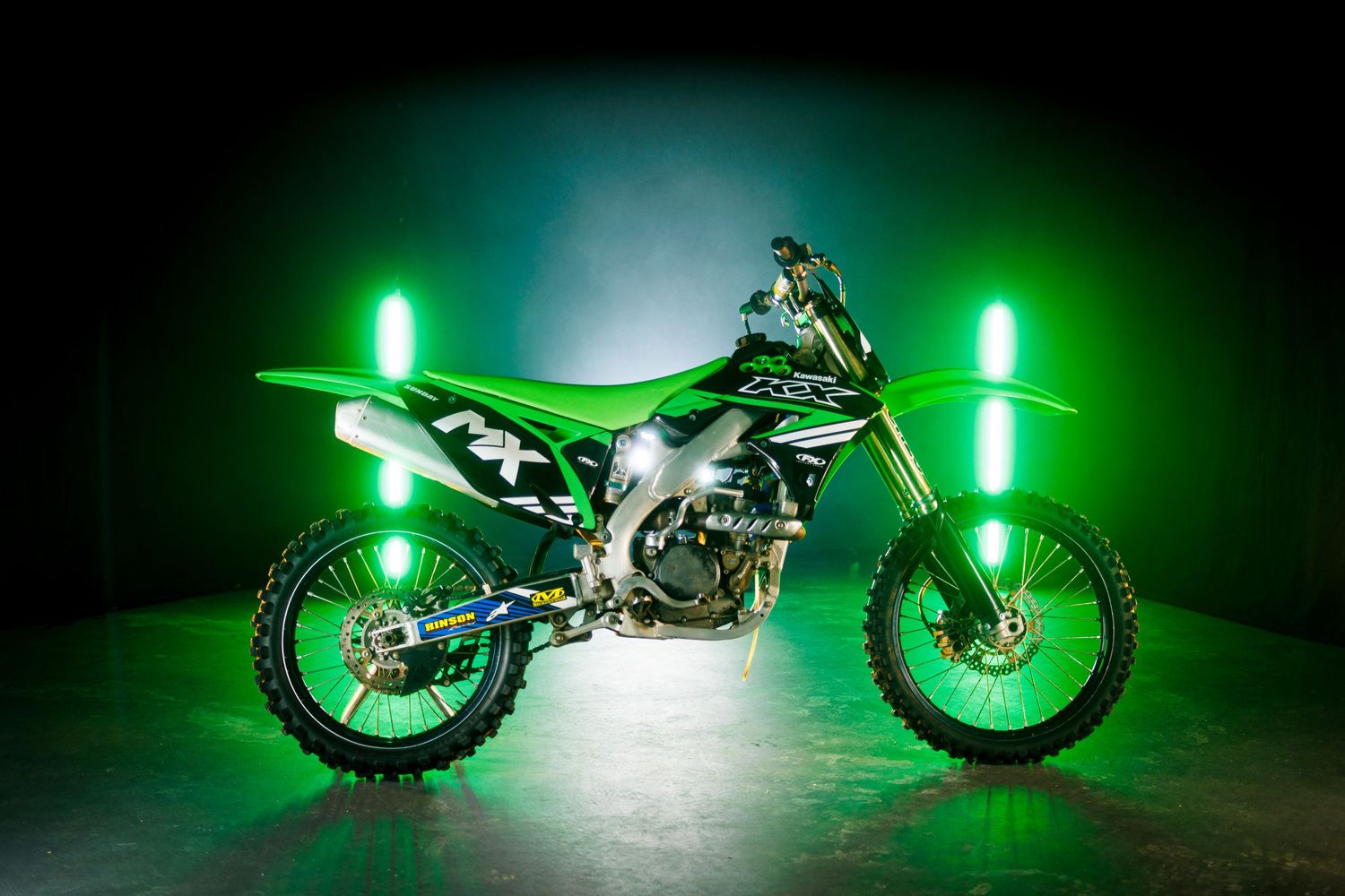 Green dirt bike illuminated by neon lights against dark background creating dramatic effect.