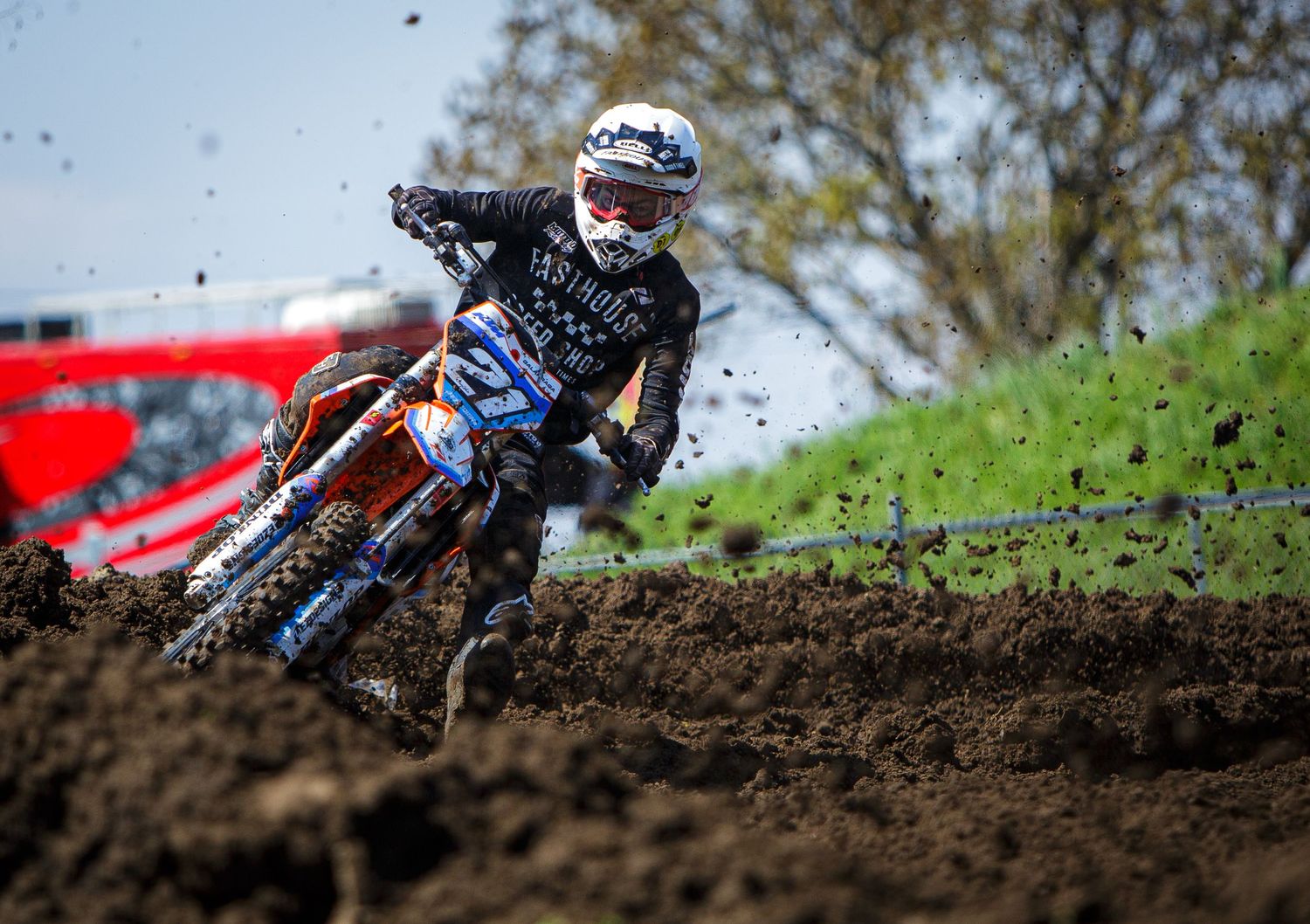 Dirt bike rider navigates muddy terrain while cornering on challenging motocross track.