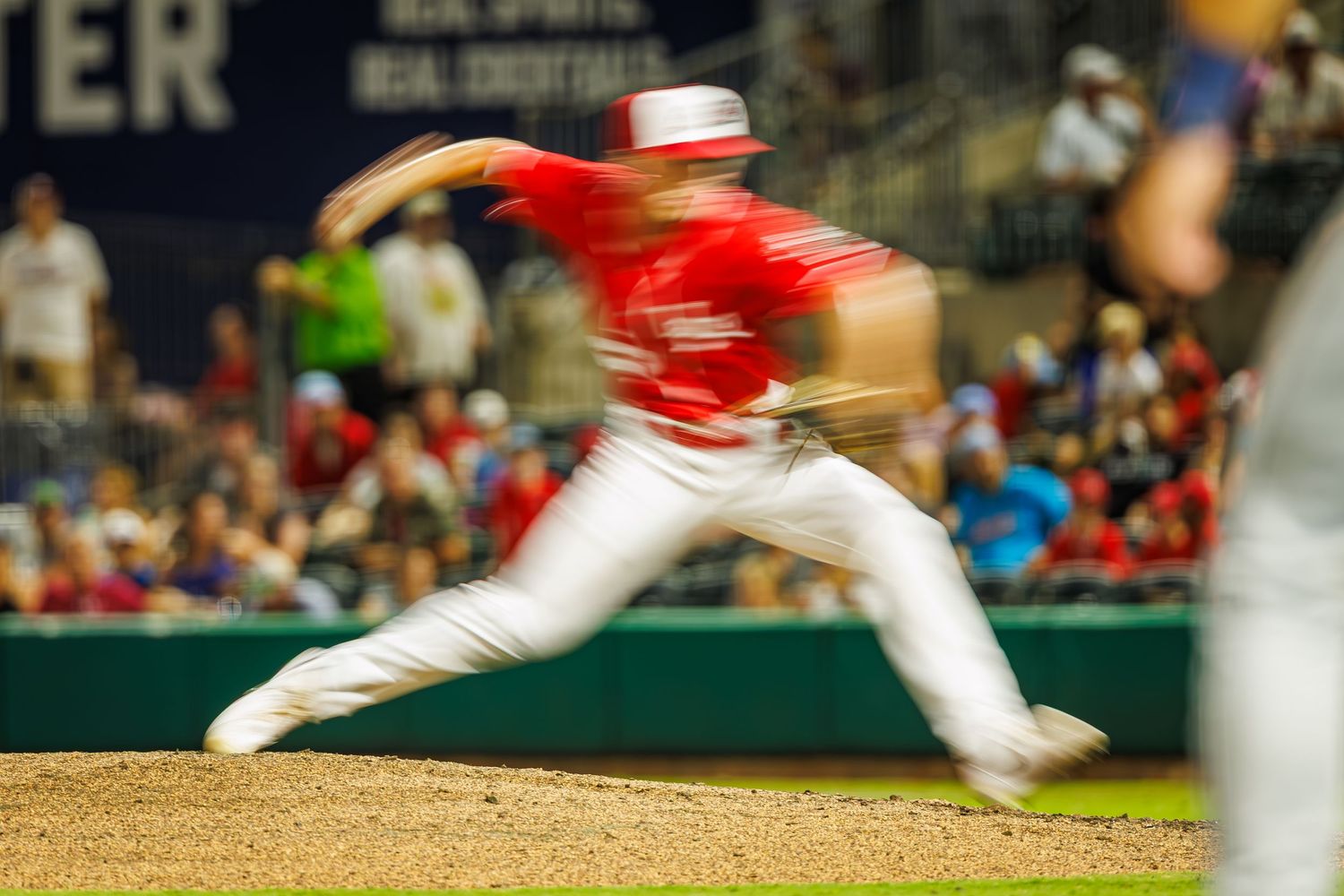 Baseball pitcher in red uniform delivers powerful throw from mound during night game at stadium.