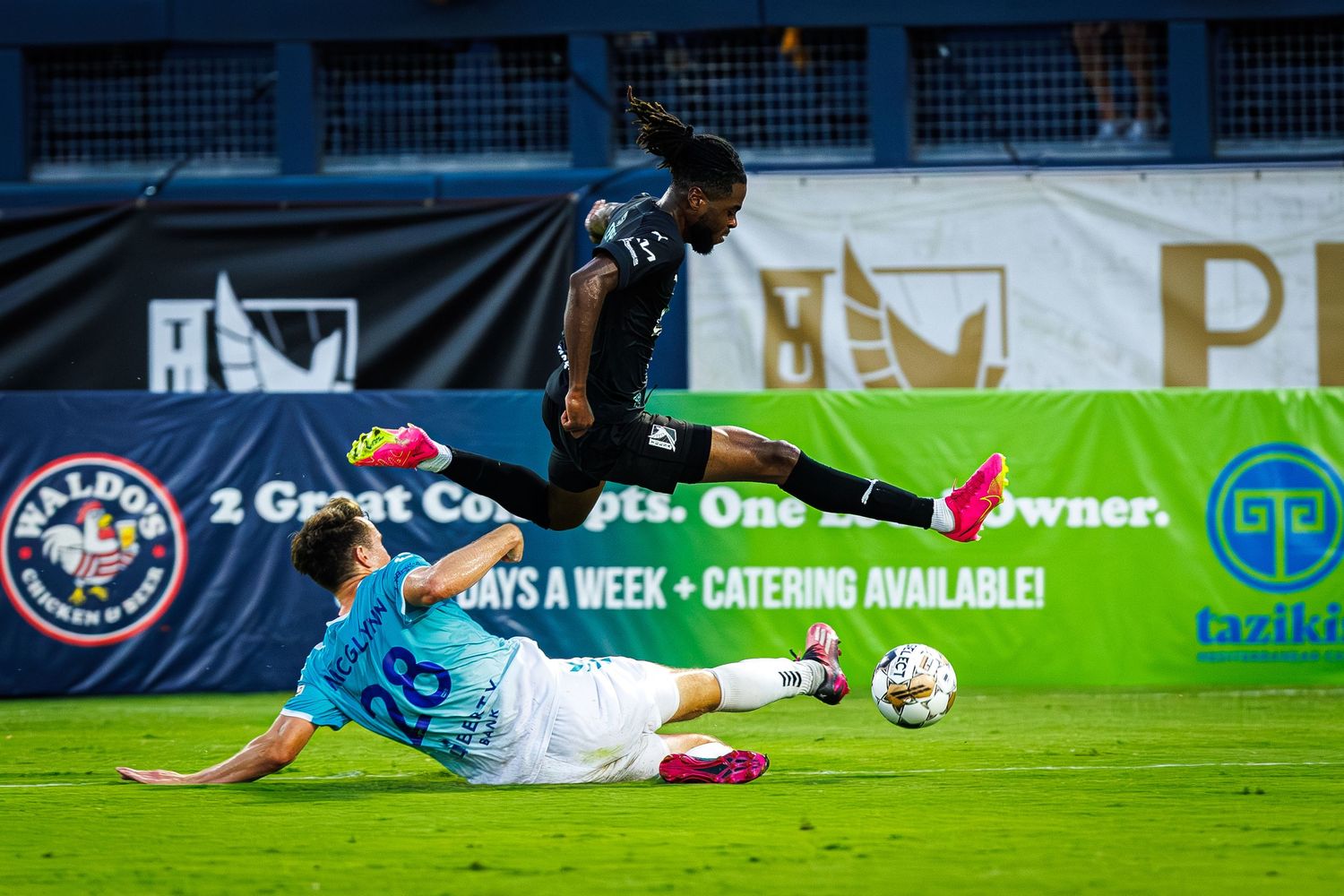 A soccer player slides on the ground during an intense match on a green turf field.