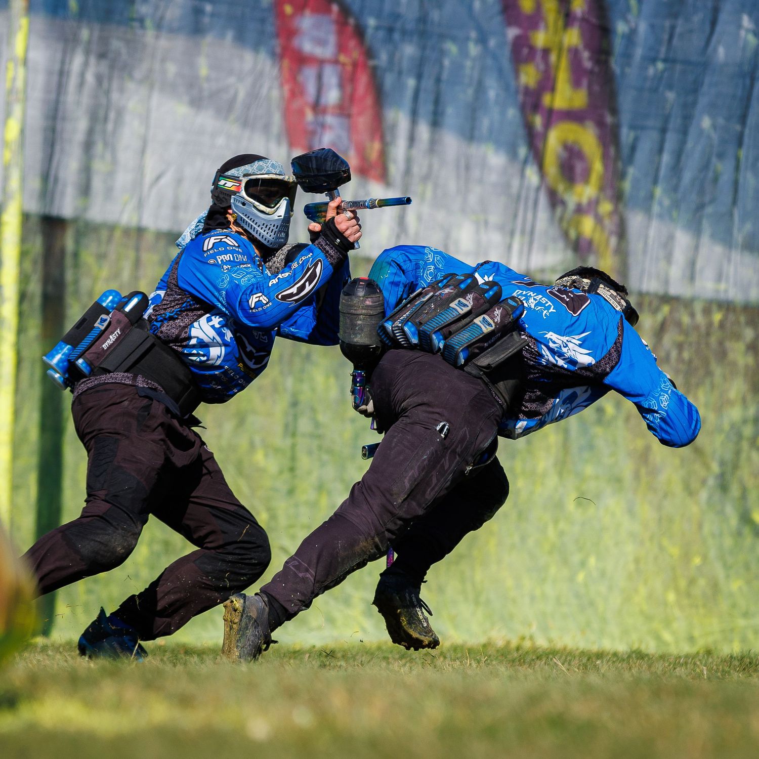 Two paintball players in blue gear moving tactically during competition.