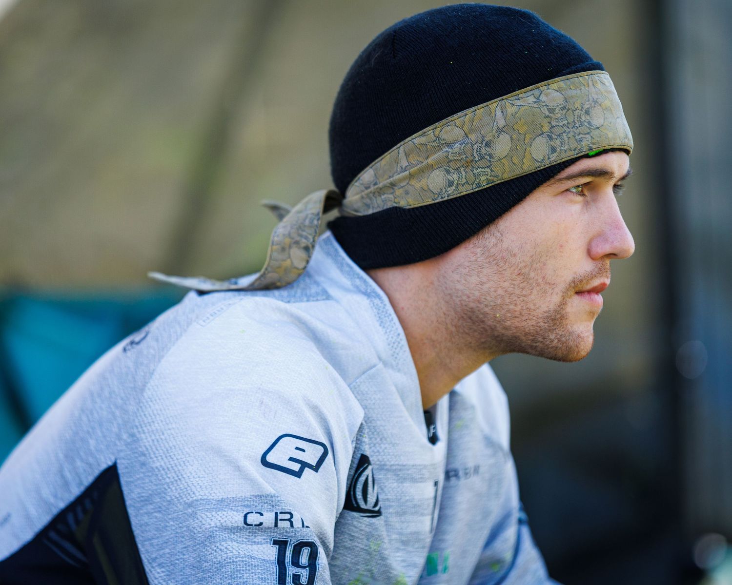 Paintball player in protective gear and beanie during competitive match.