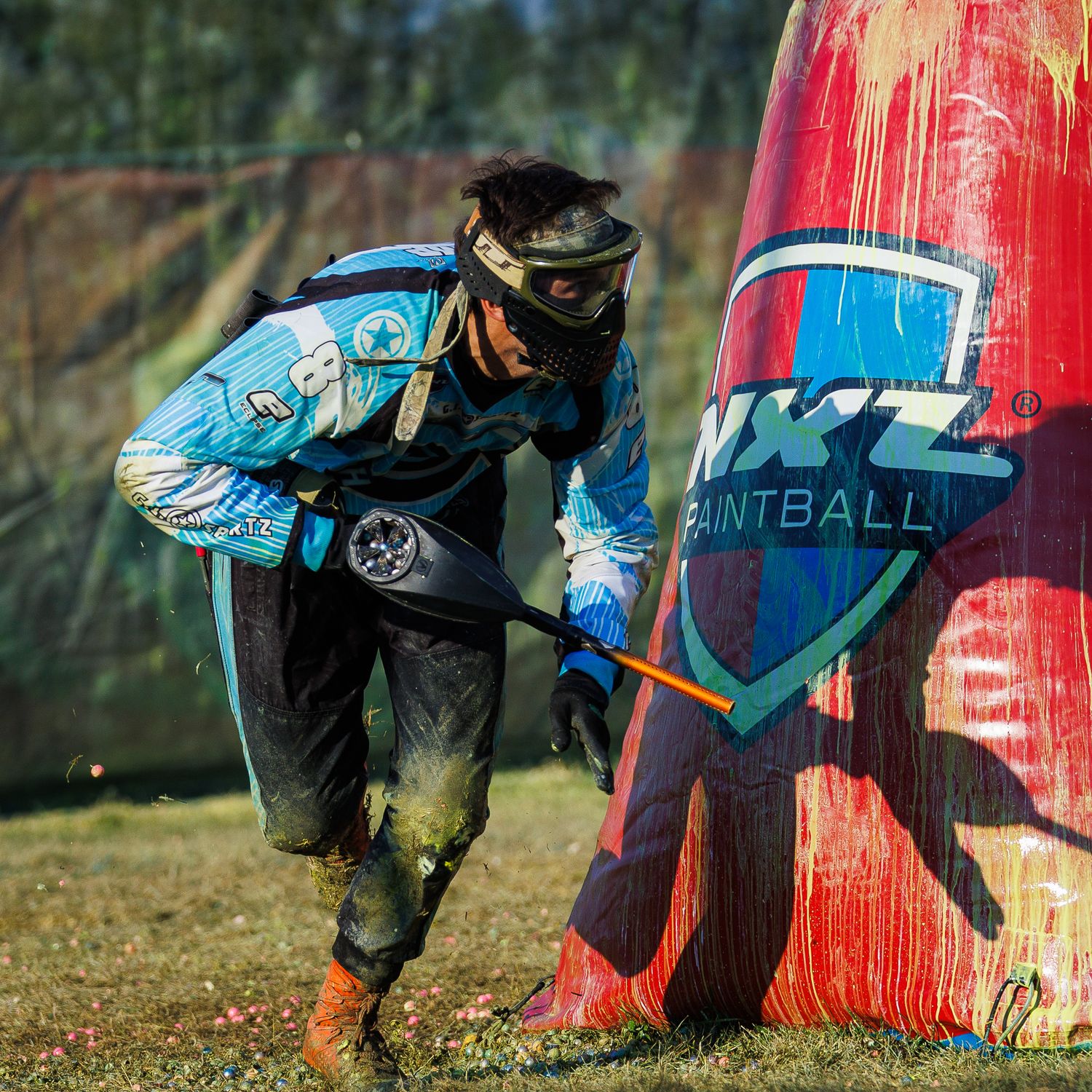 Competitive paintball player moves swiftly behind blue and red bunkers during tournament play.