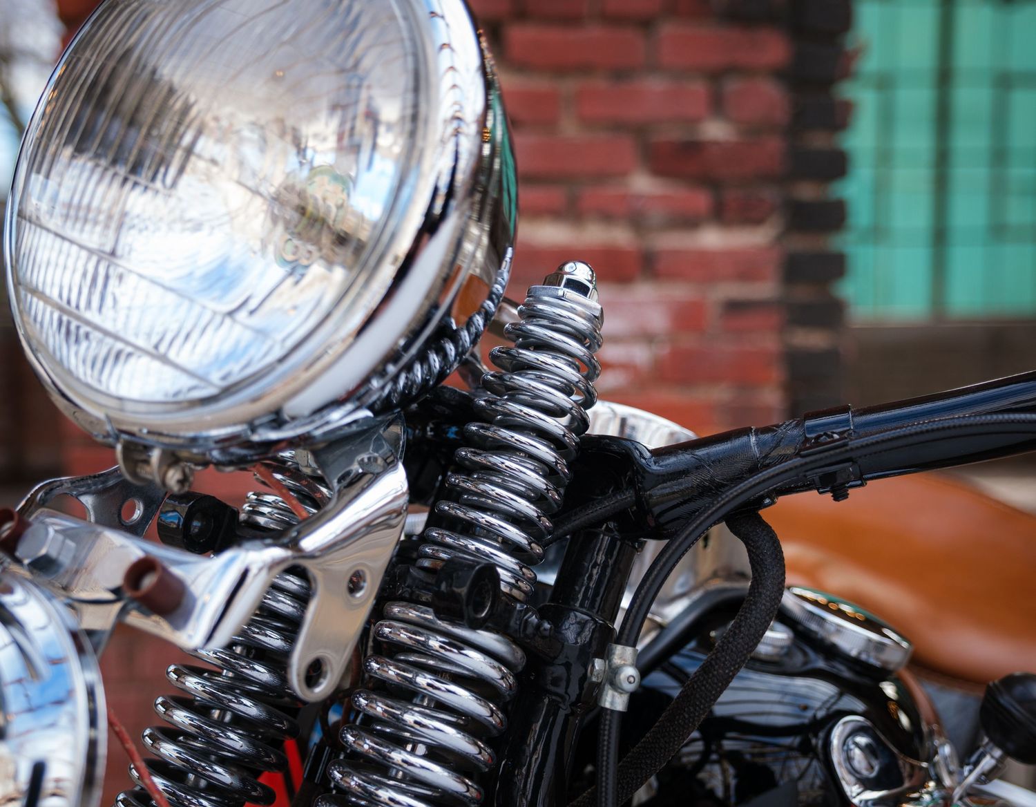 Vintage motorcycle headlight with exposed suspension springs against a brick wall background.