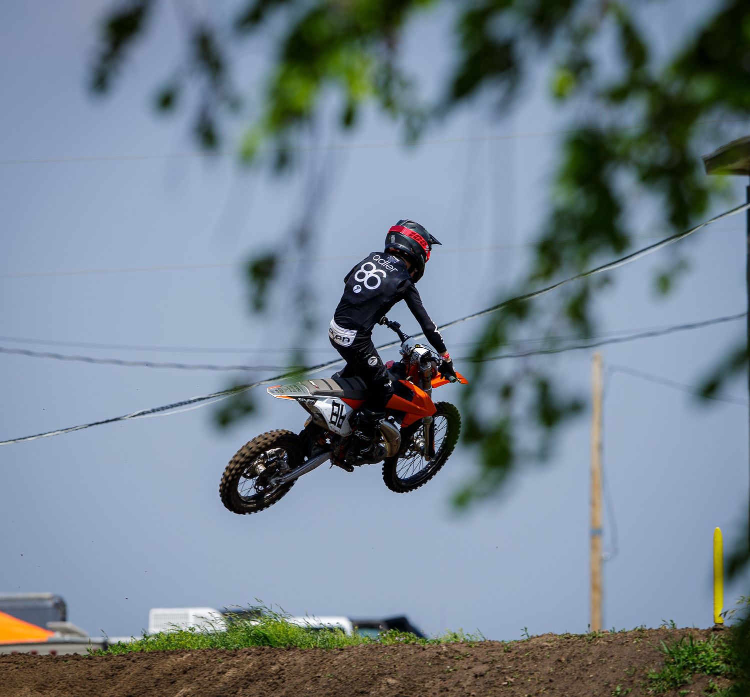 A motocross rider performs a dramatic jump against an overcast sky during competition.
