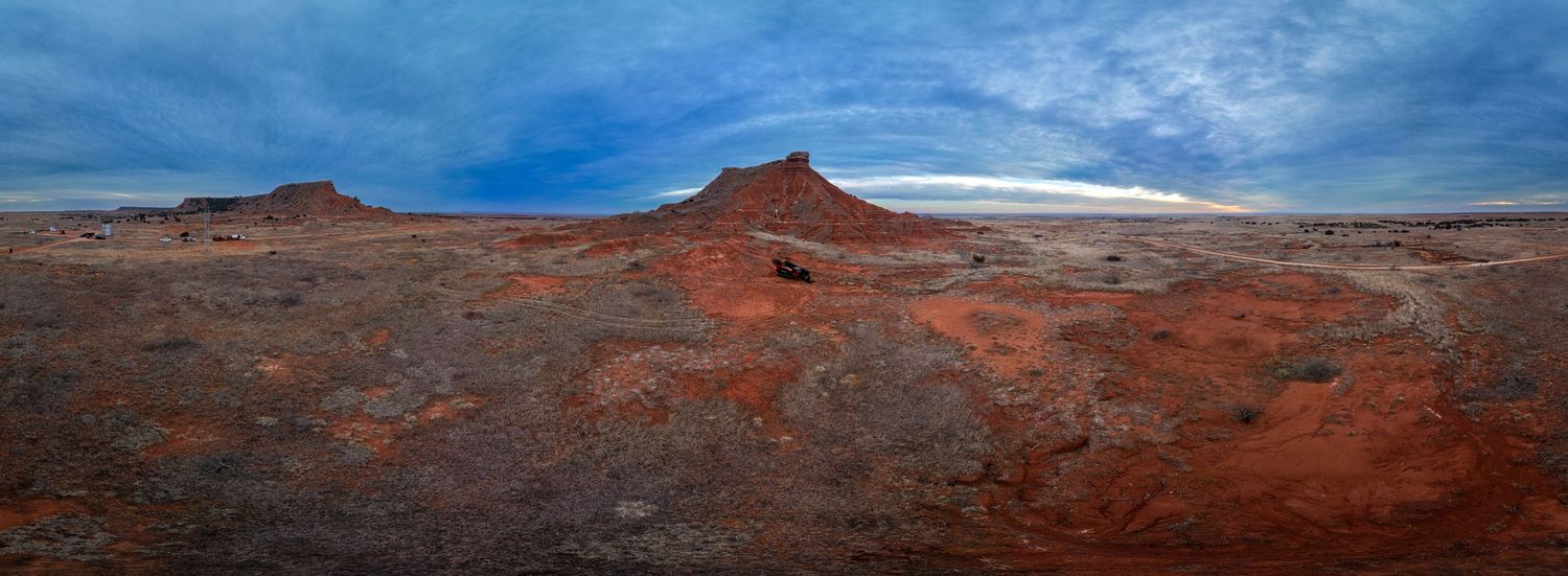 Red rock desert landscape under blue sky with dramatic rock formations in panoramic view.