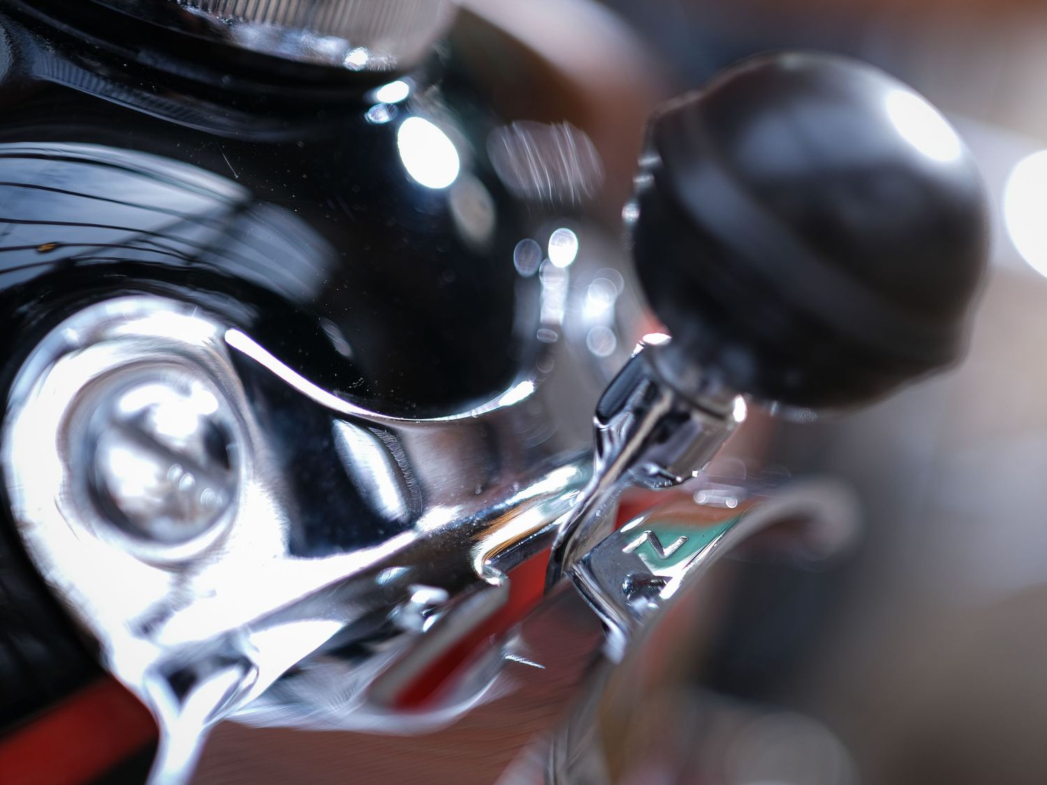 Chrome motorcycle handlebar control with black grip in shallow focus.