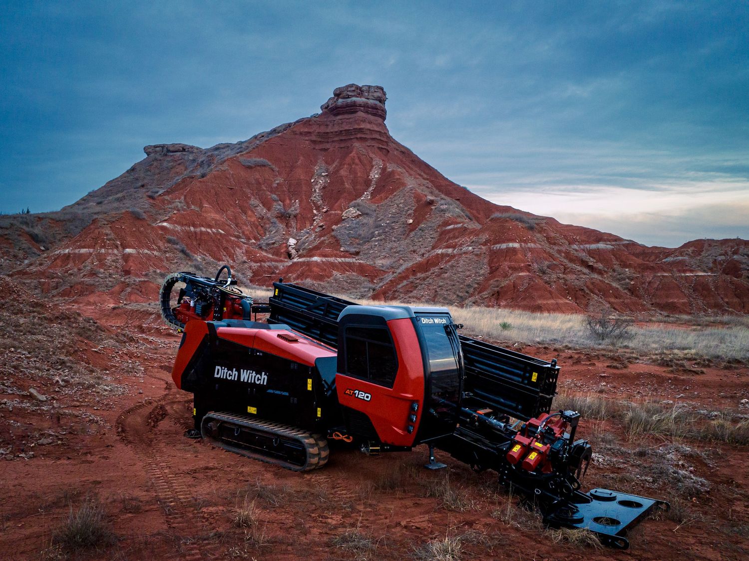 Red camping vehicle parked near dramatic red rock formations in a desert landscape.