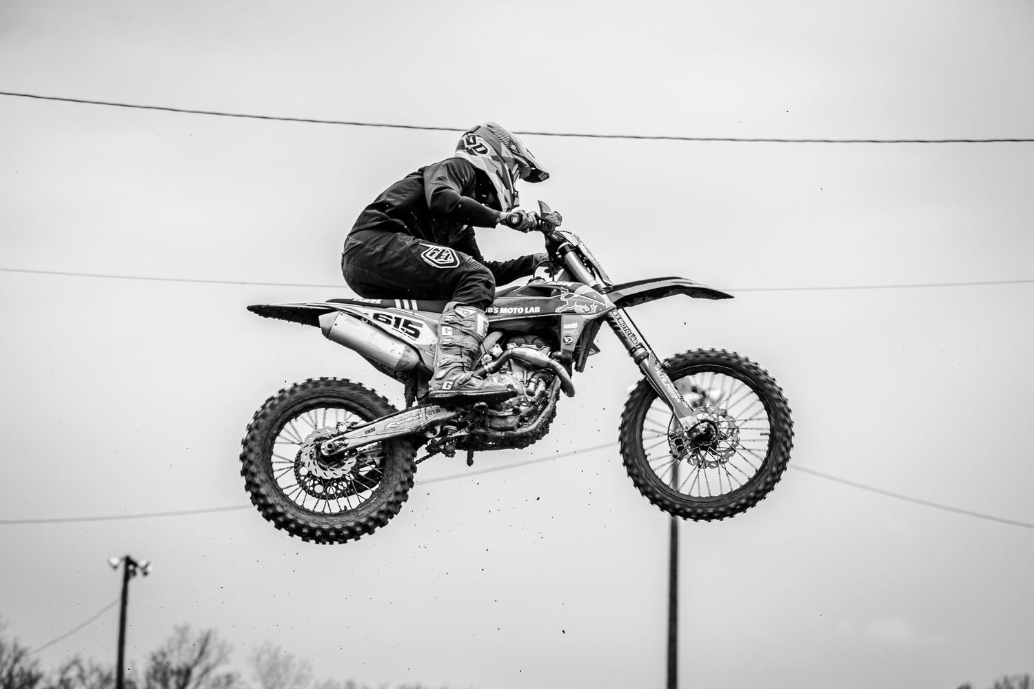 A motocross rider performs a dramatic jump on a dirt bike against an overcast sky.