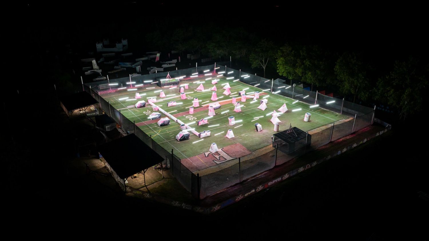 Aerial night view of illuminated sports field with multiple white tent structures.