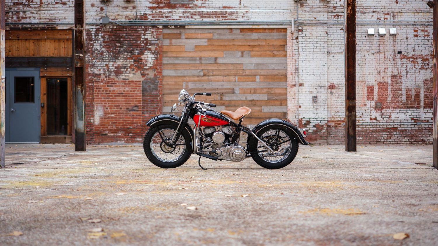 Wide panoramic shot of vintage motorcycles lined up against distressed industrial brick wall.