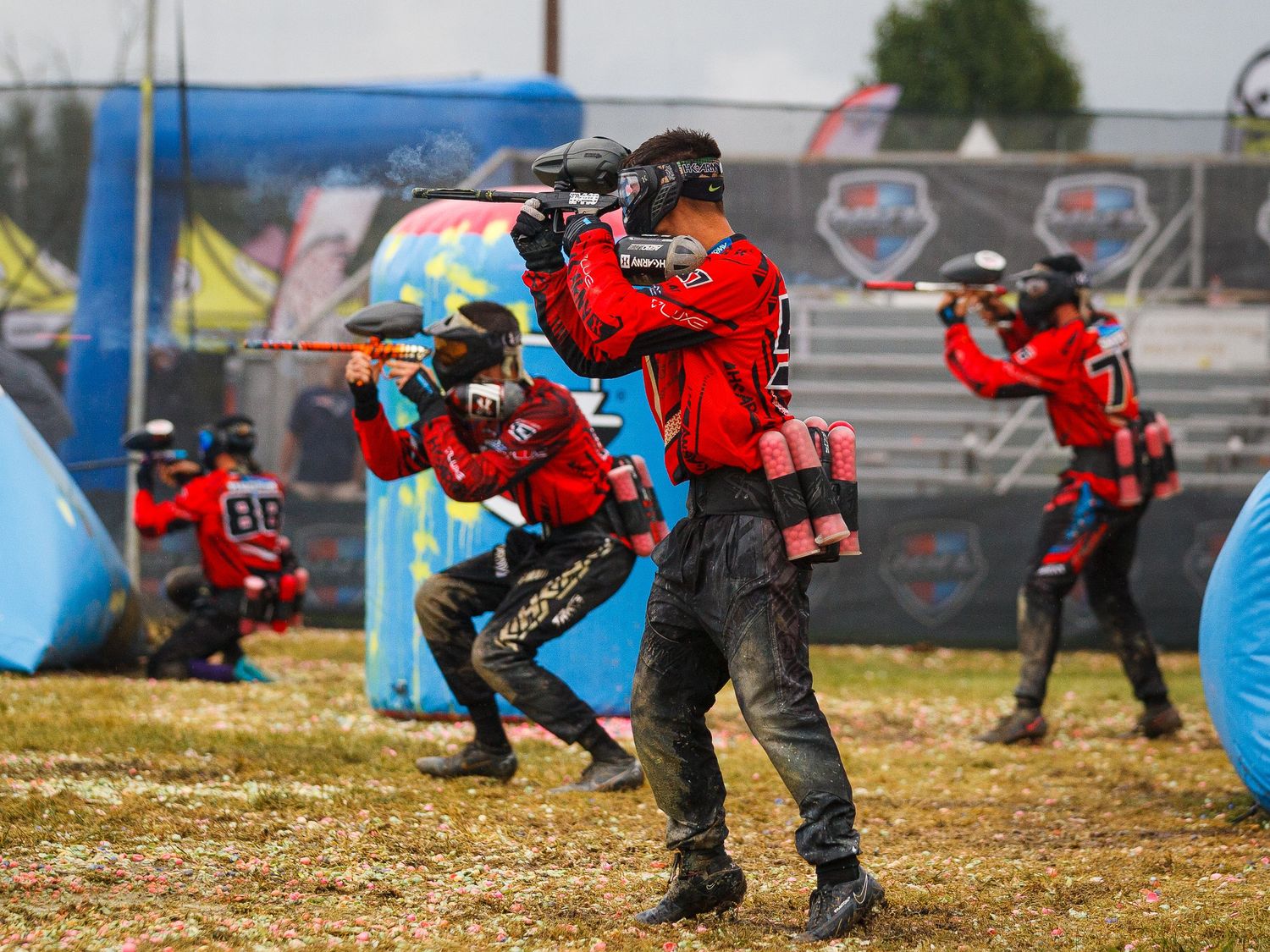 Team of paintball players in red jerseys line up to shoot during competitive match.