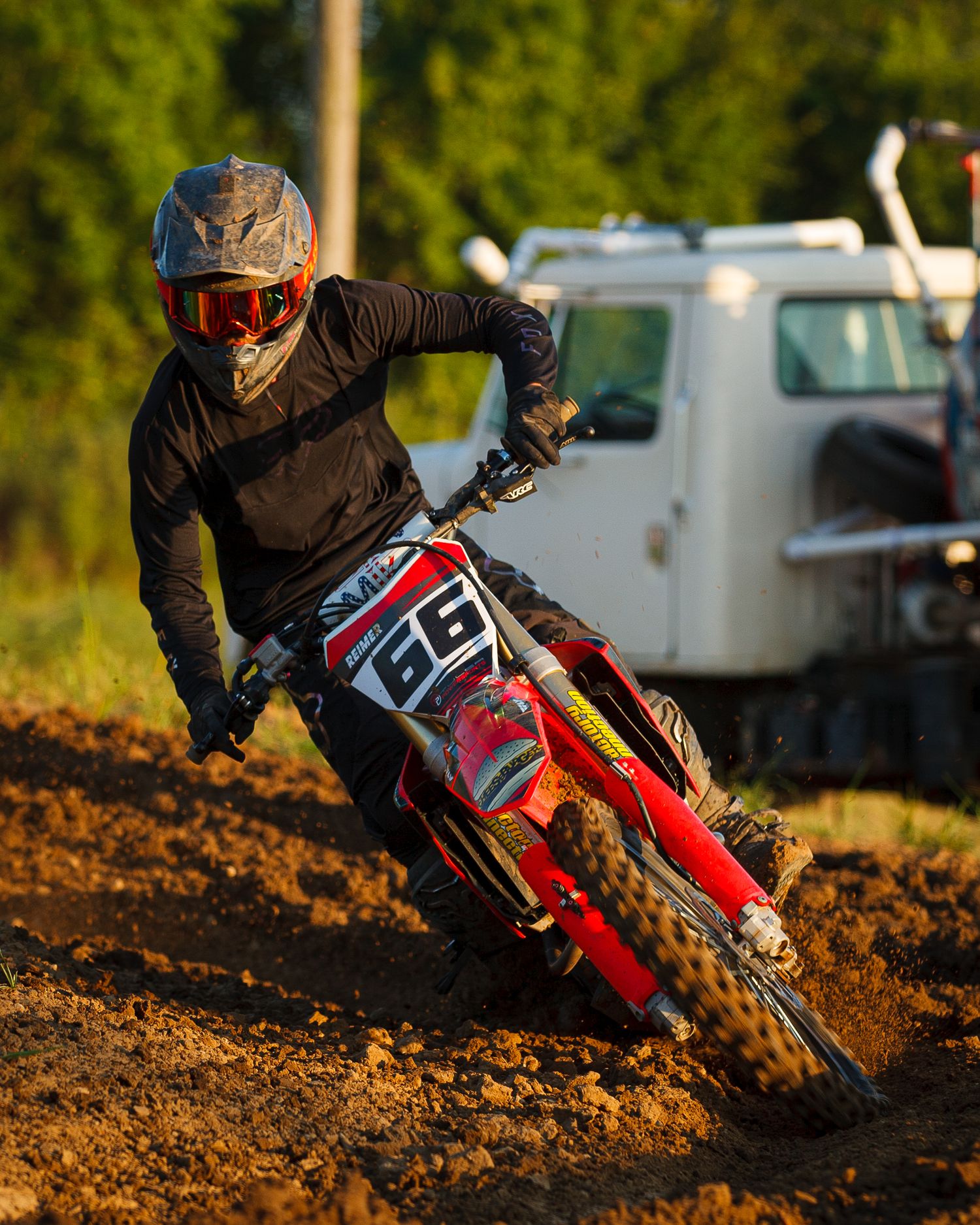 Motocross rider leans into a turn on red dirt bike during competitive race.