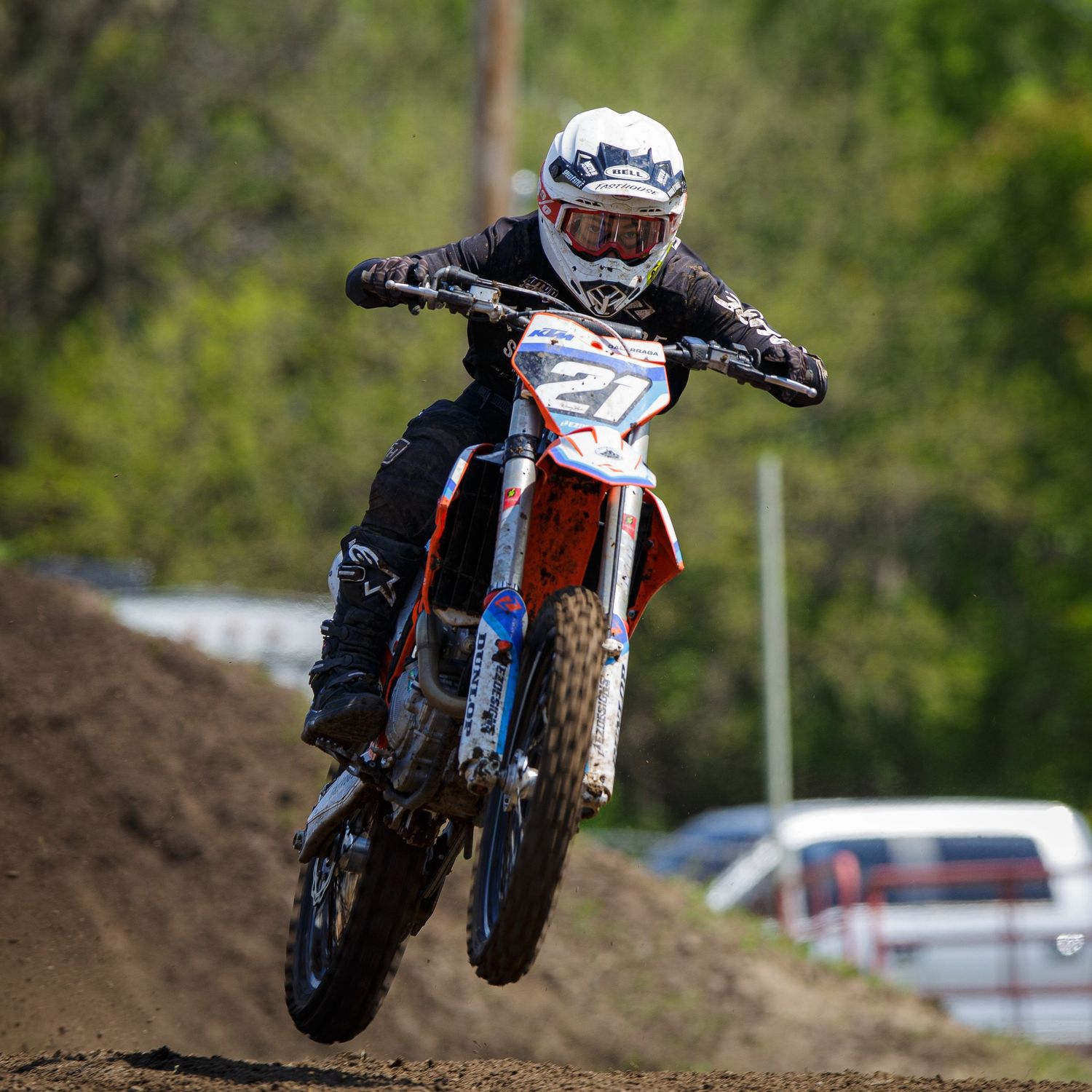 Motocross rider launches dirt bike over jump on outdoor racing track.