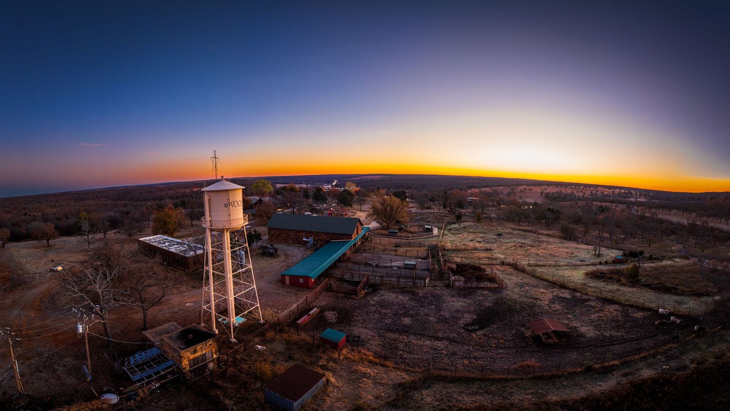 Panoramic sunset view of rural landscape with water tower silhouetted against orange sky.