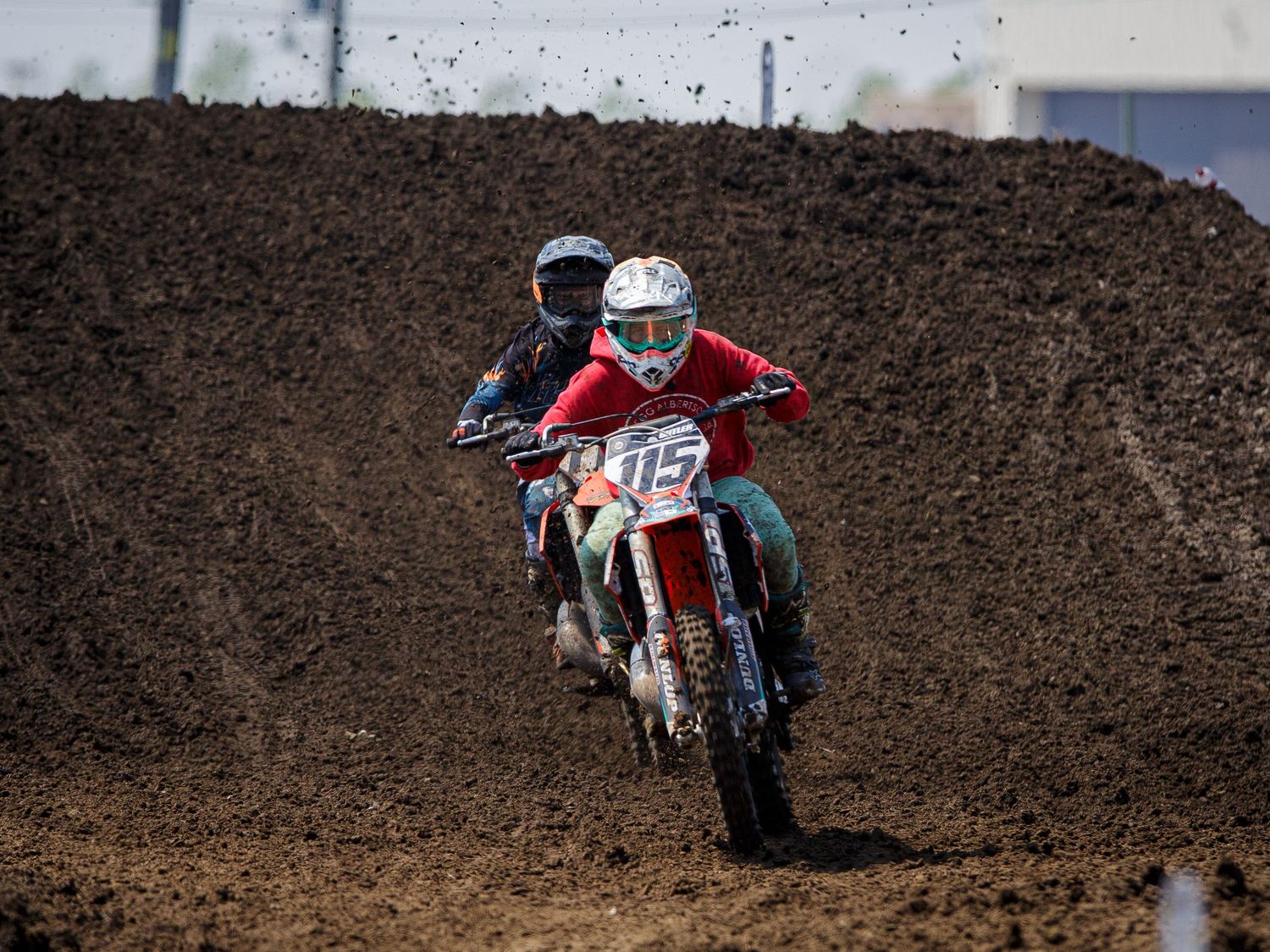 Two dirt bike riders navigate steep hill during intense motocross race.