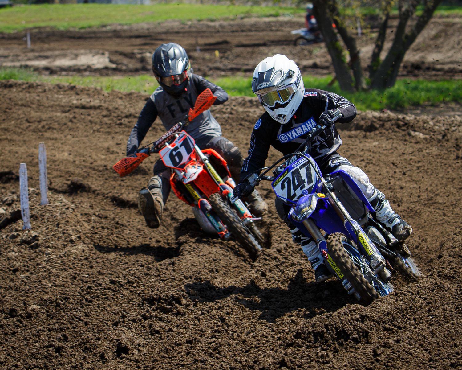 Two motocross riders battle for position while cornering on dirt track.
