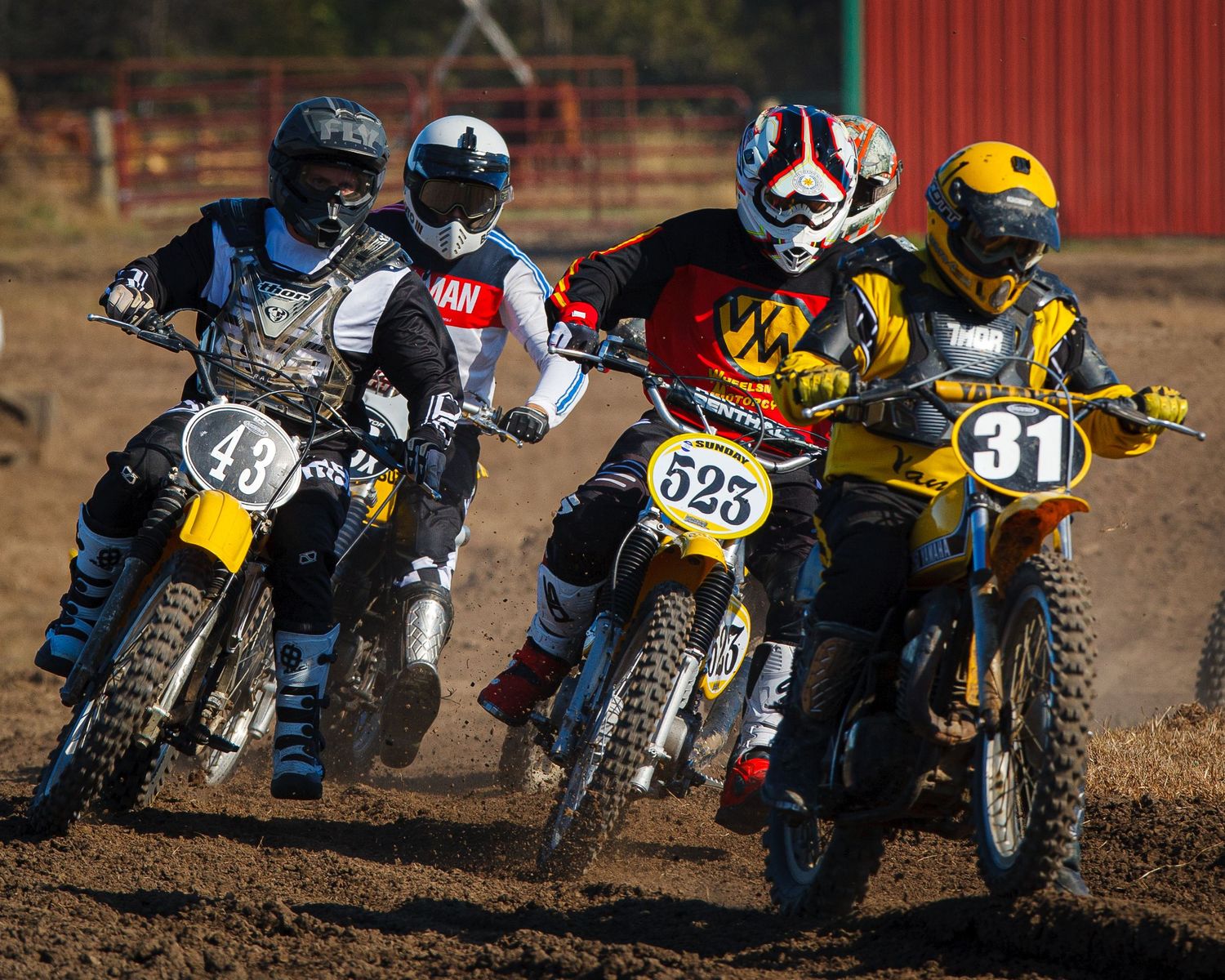 Group of motocross riders racing side by side on muddy dirt track during competition.