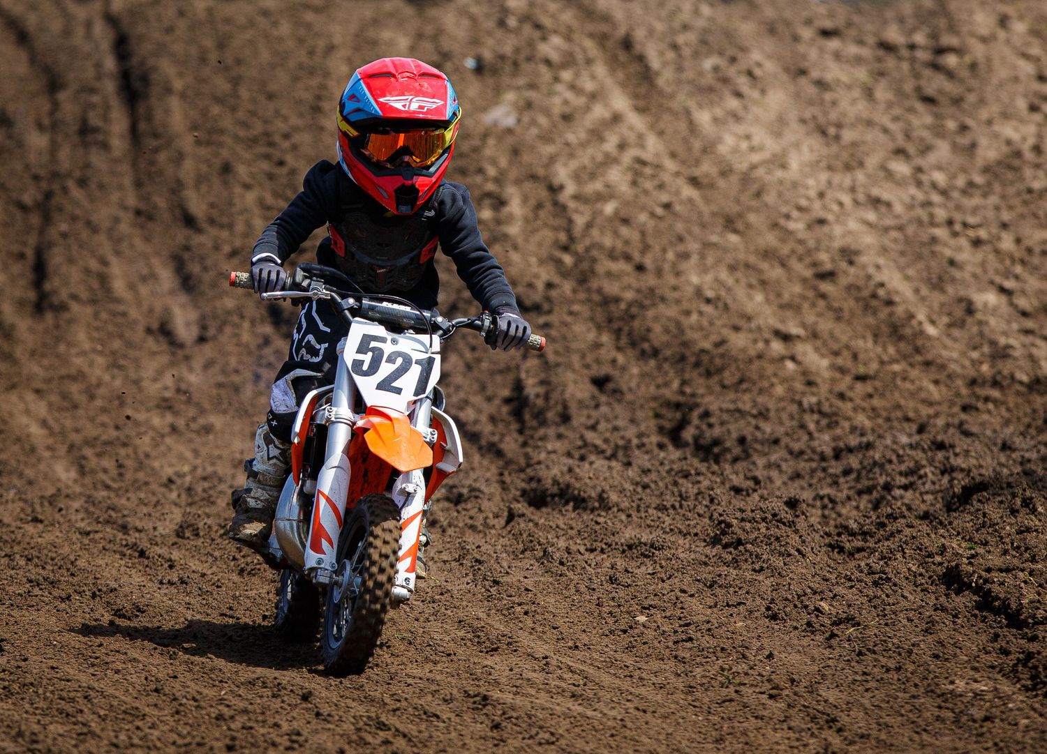 Dirt bike racer navigates a muddy motocross track with intense focus in racing gear.