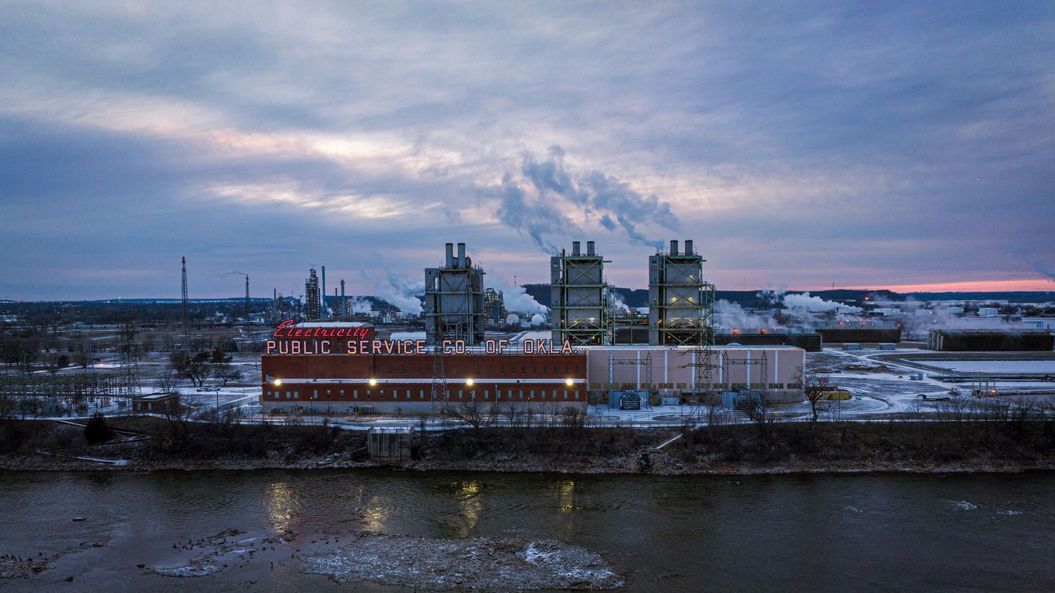 Industrial waterfront facility with storage tanks and buildings during sunset.