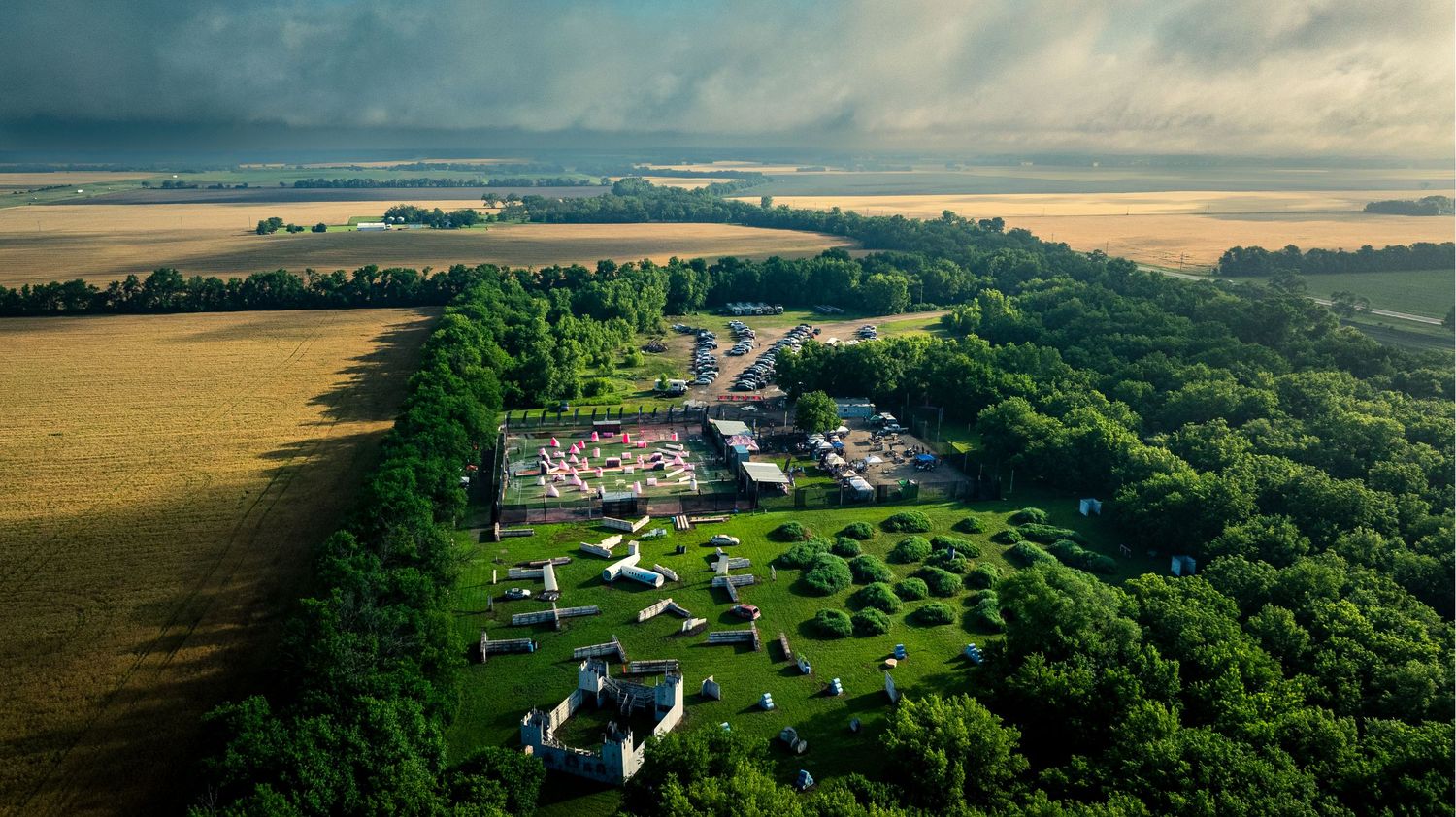 Aerial panoramic view of rural countryside with green forests, farmland and scattered buildings under dramatic sky.
