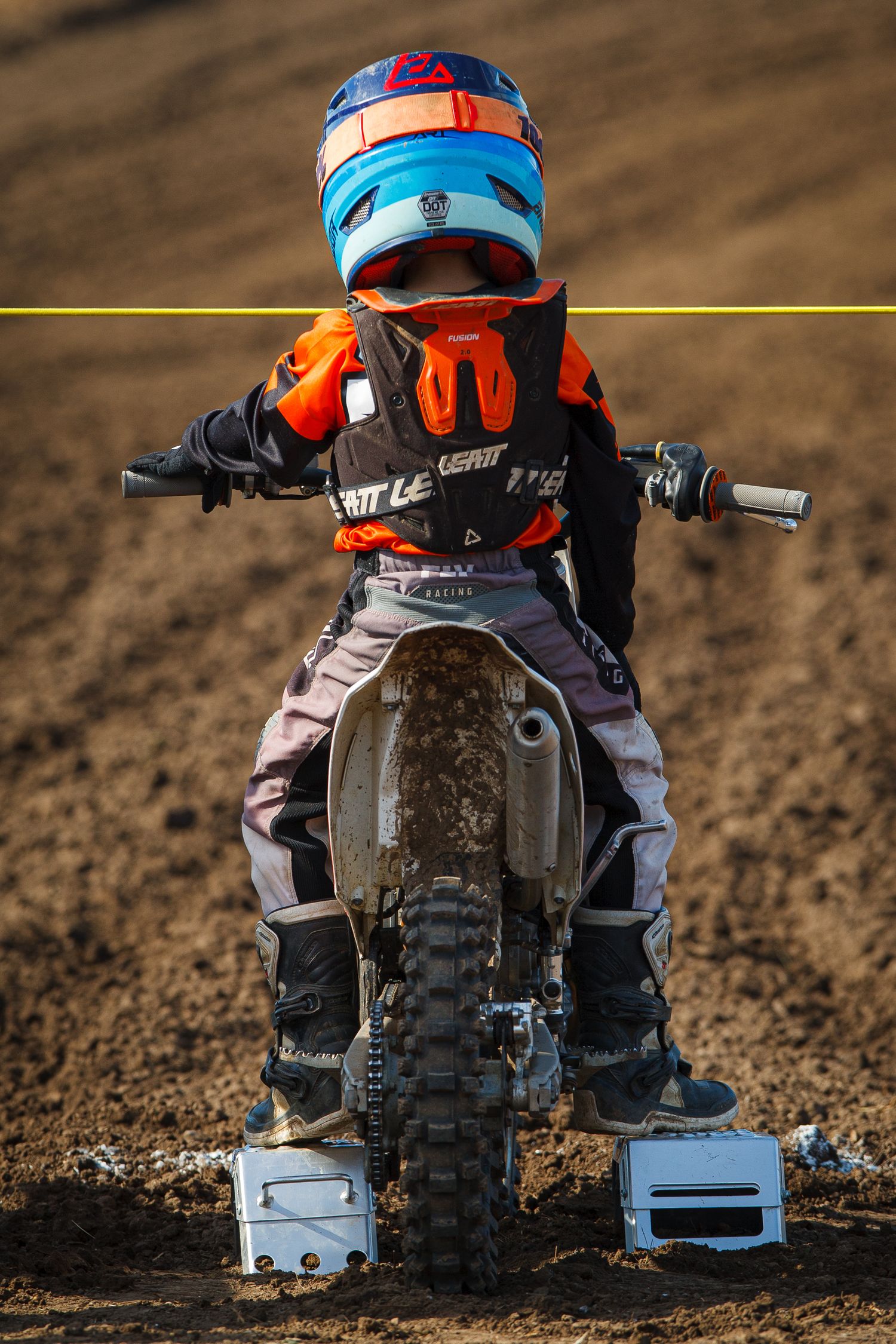 Young dirt bike rider in colorful protective gear and helmet riding on a muddy track.