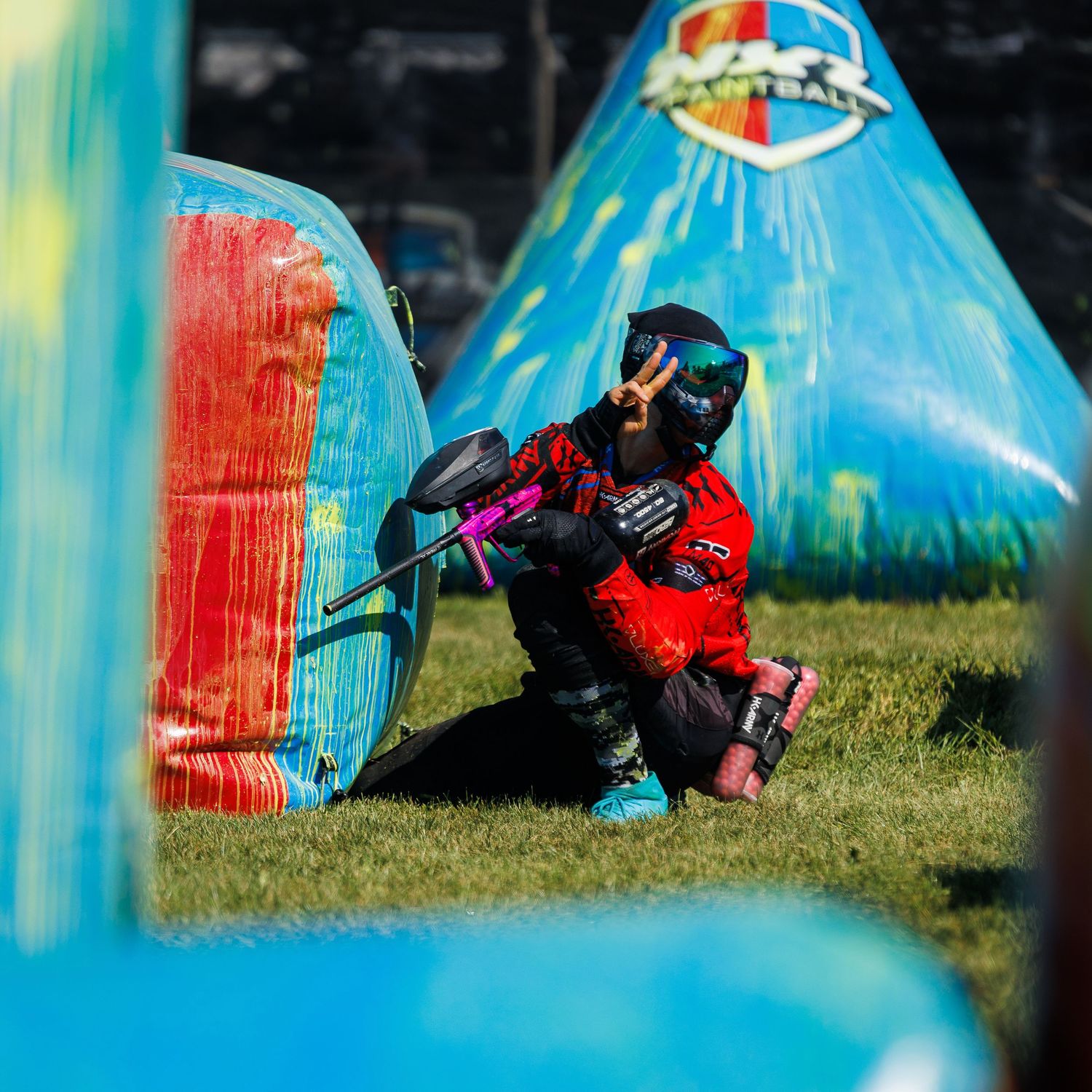 A paintball player takes aim from behind a blue bunker during a competitive match.
