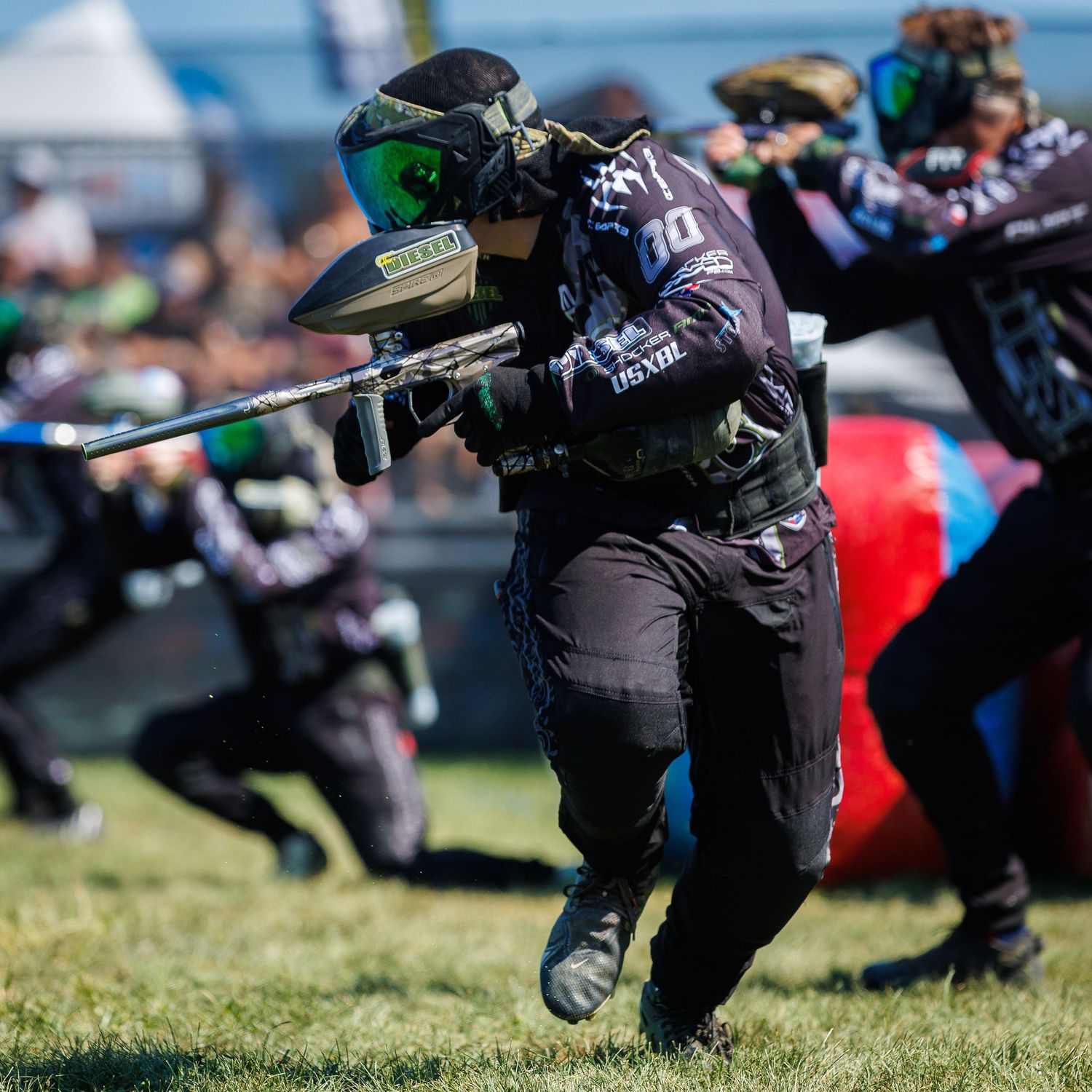 Paintball player in dark gear aiming marker during competitive speedball game.