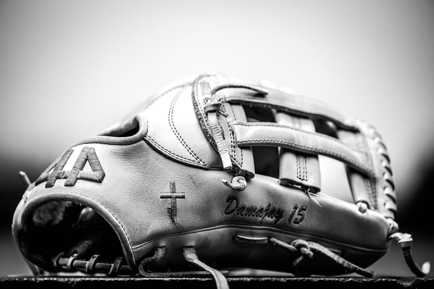 A black and white close-up photograph of a worn leather baseball glove showing detailed stitching and texture.