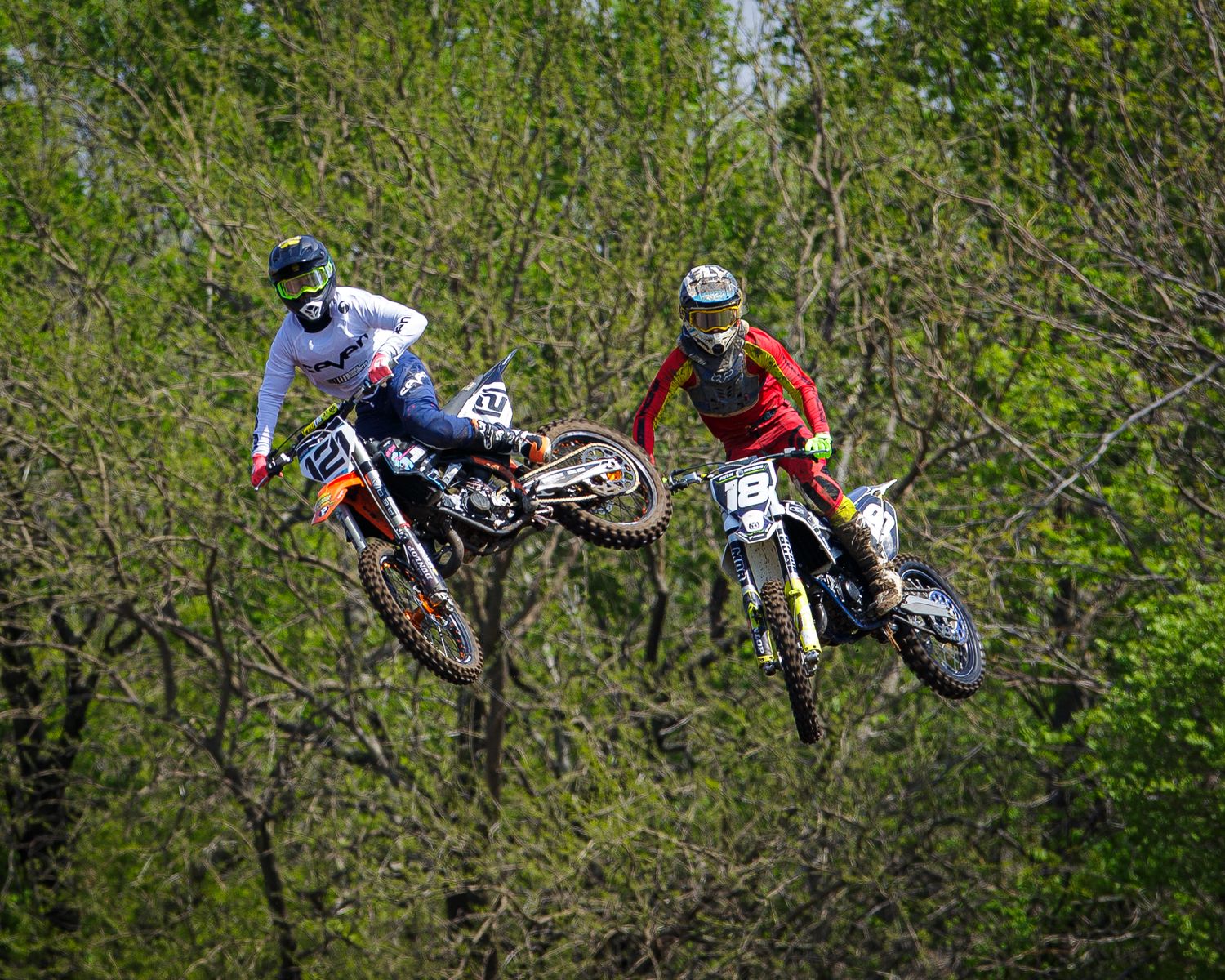 Two motocross racers leap simultaneously through the air during an intense competition.