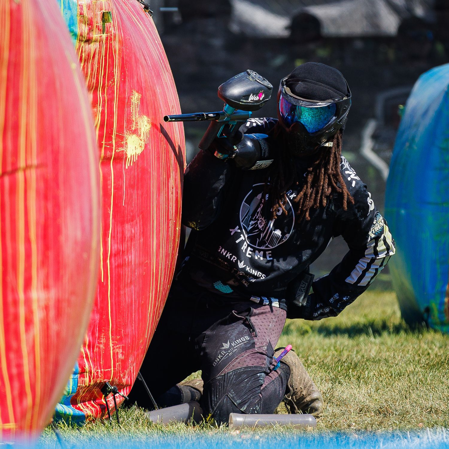 Paintball competitor in black gear taking cover behind red inflatable bunker.