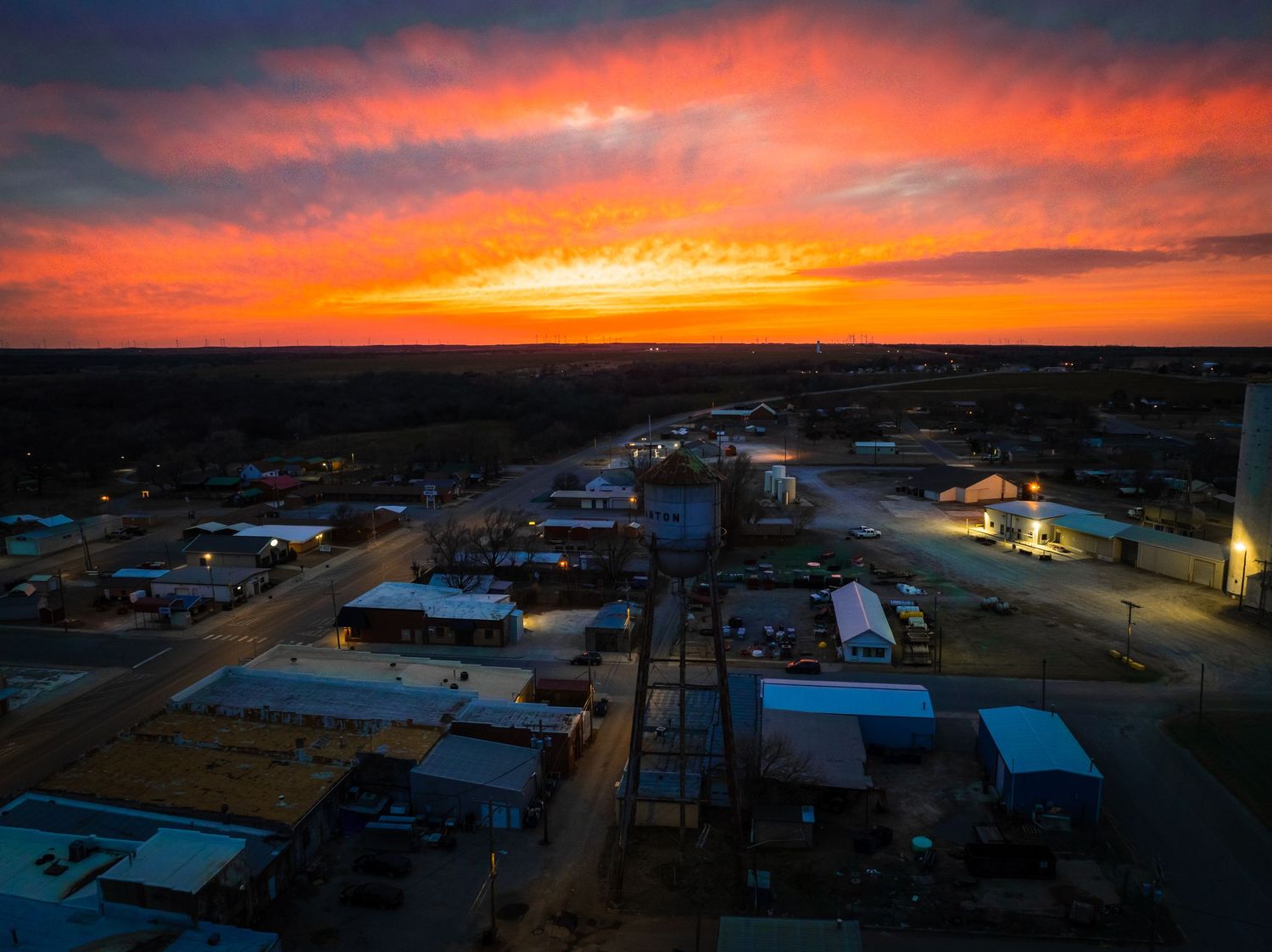 Aerial view of small town streets and buildings illuminated at dusk with orange sky.