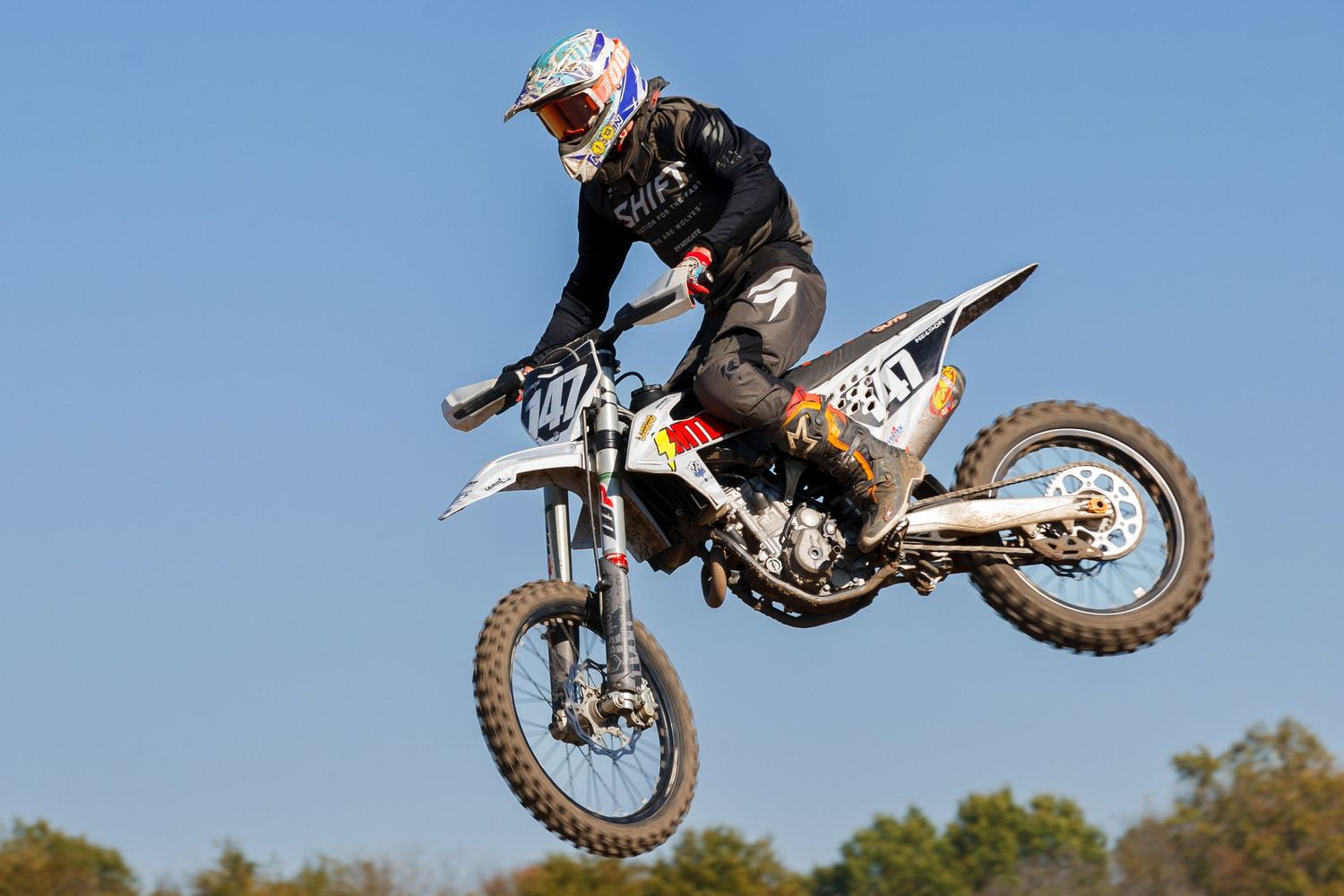 Dirt bike rider executes dramatic jump during motocross competition.