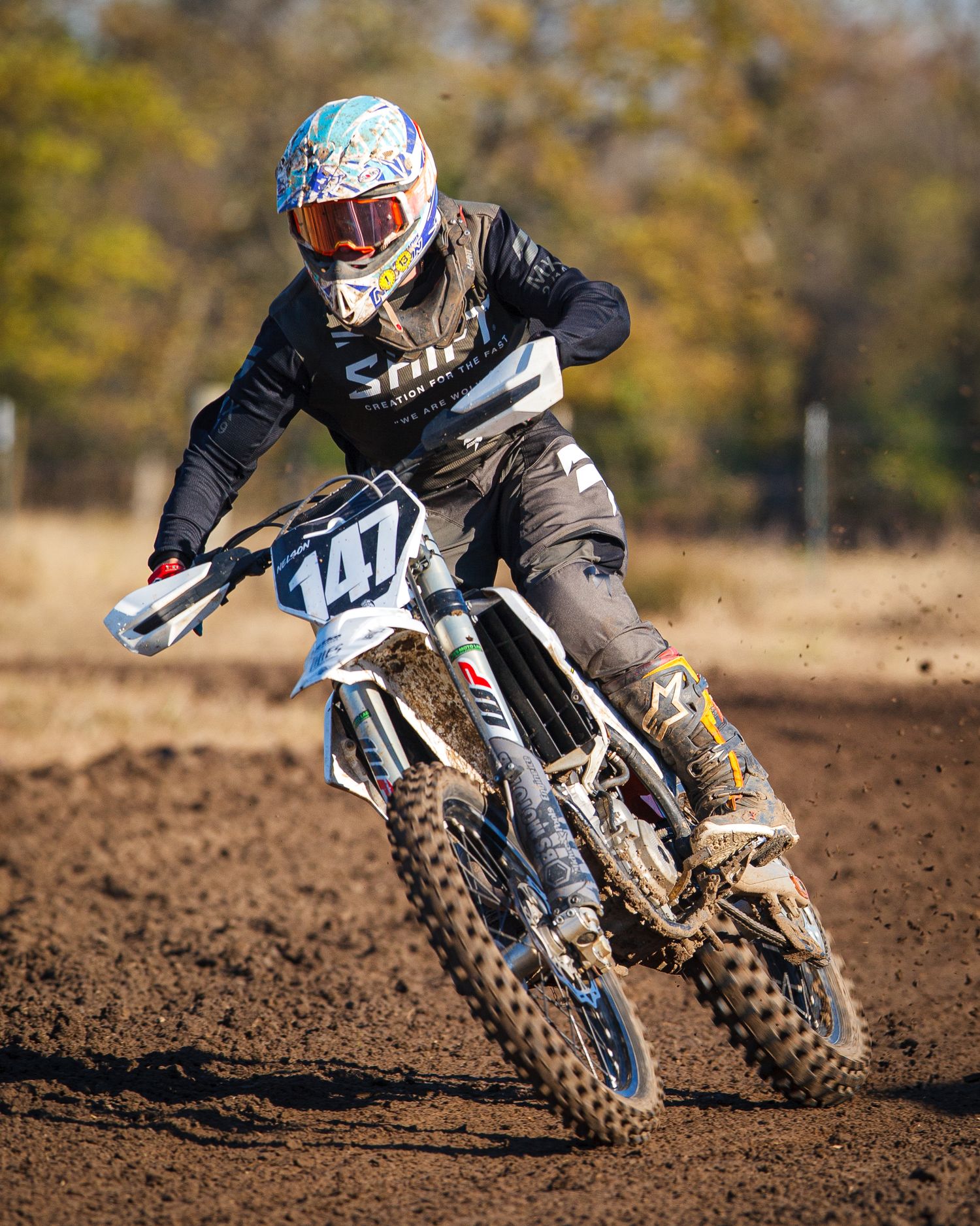 Rider maneuvers dirt bike through corner on muddy motocross track.