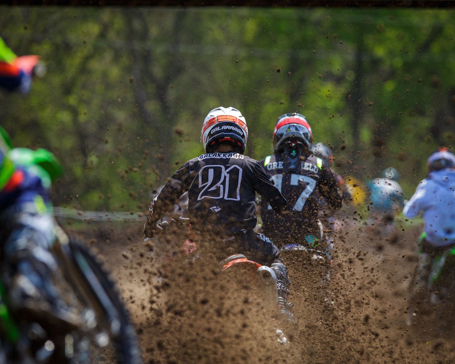 Dirt bike racers kick up mud while competing on a motocross track during an intense race.