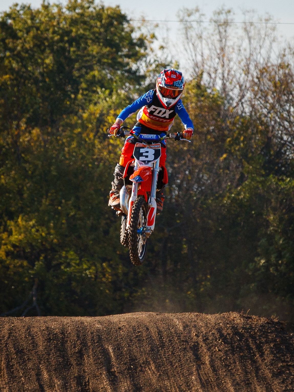 Orange dirt bike catching air over jump during motocross race.