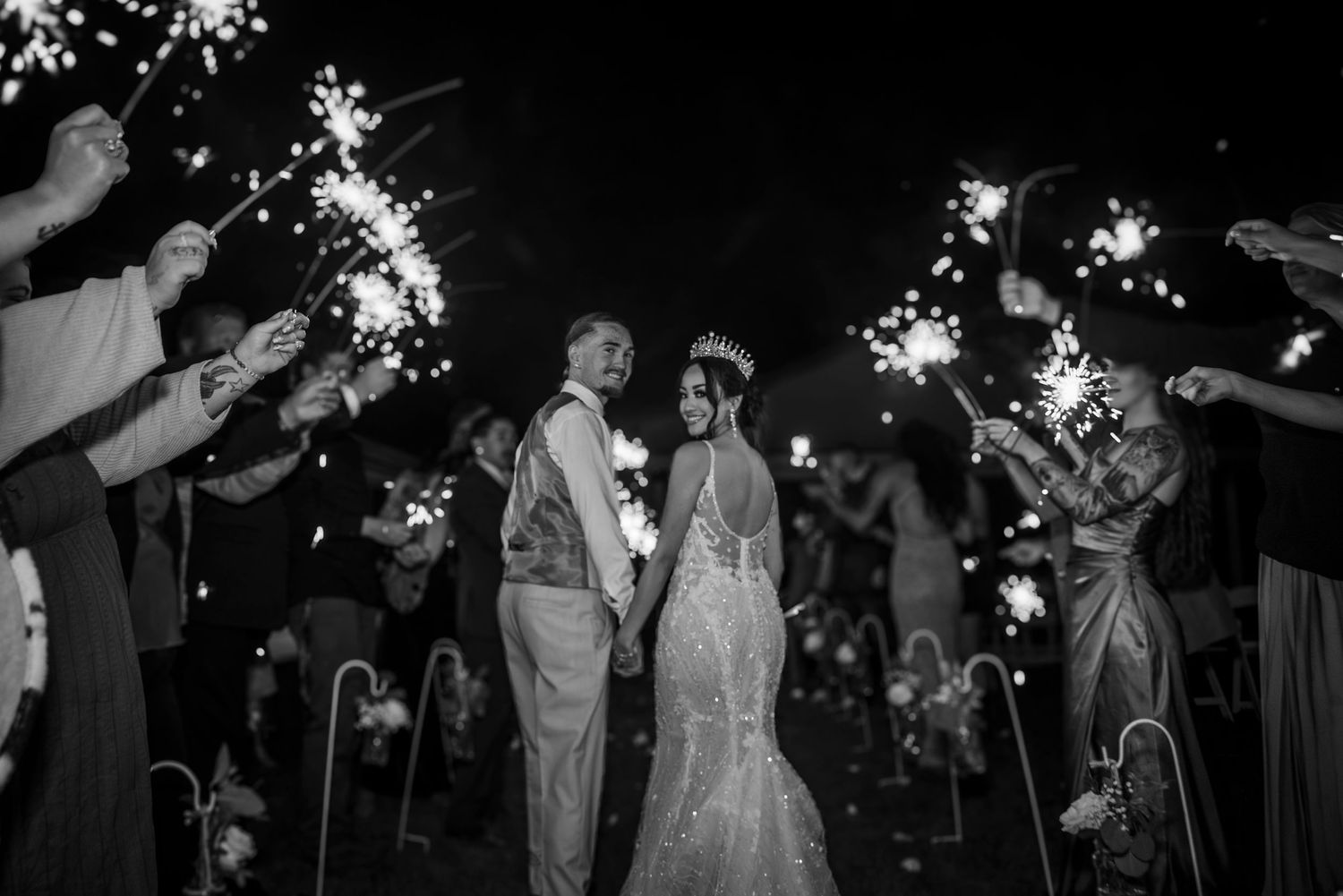 A couple shares a romantic moment under sparklers held by wedding guests in this elegant black and white photograph.