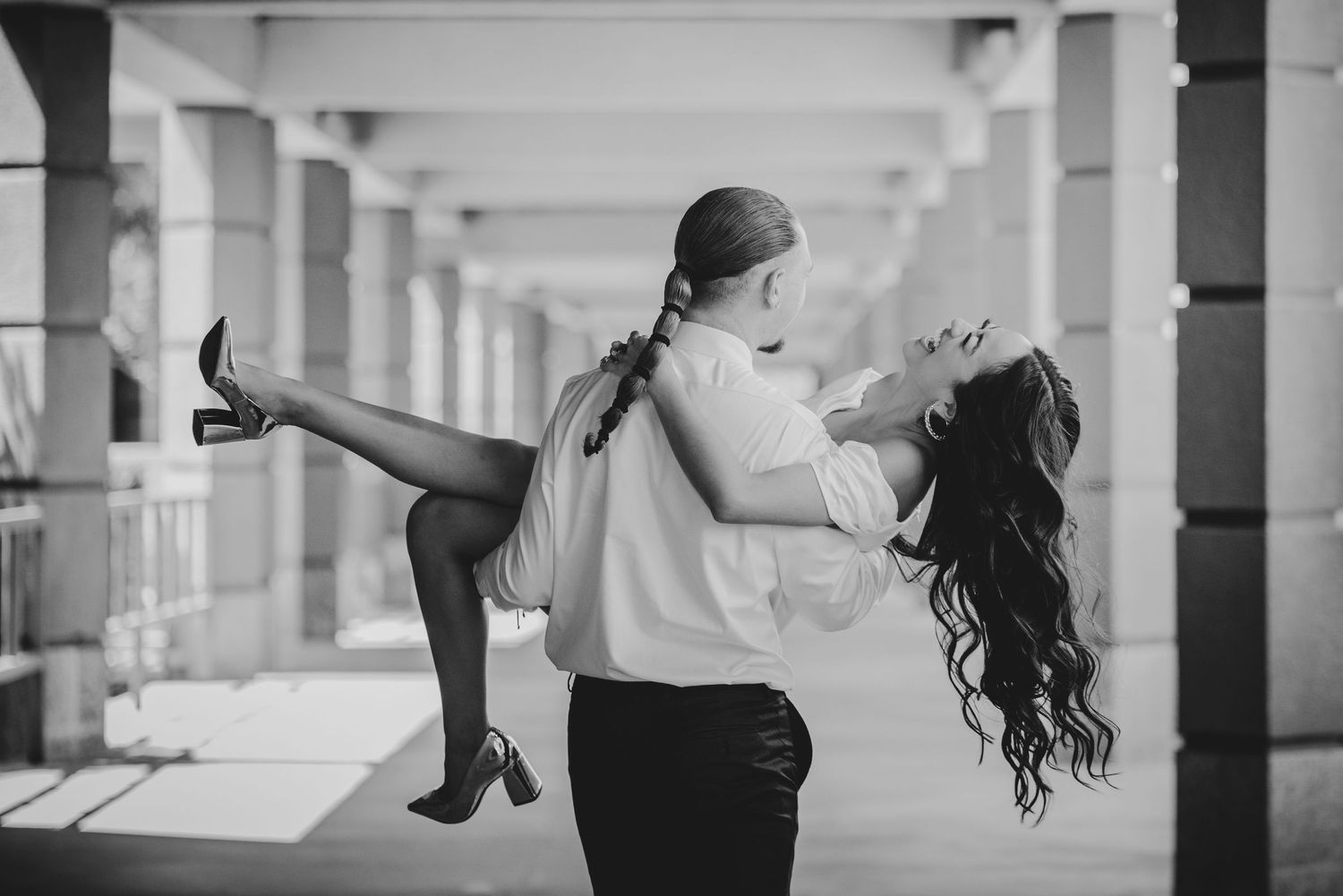 A black and white romantic capture showing two people dancing in an elegant corridor with columns.