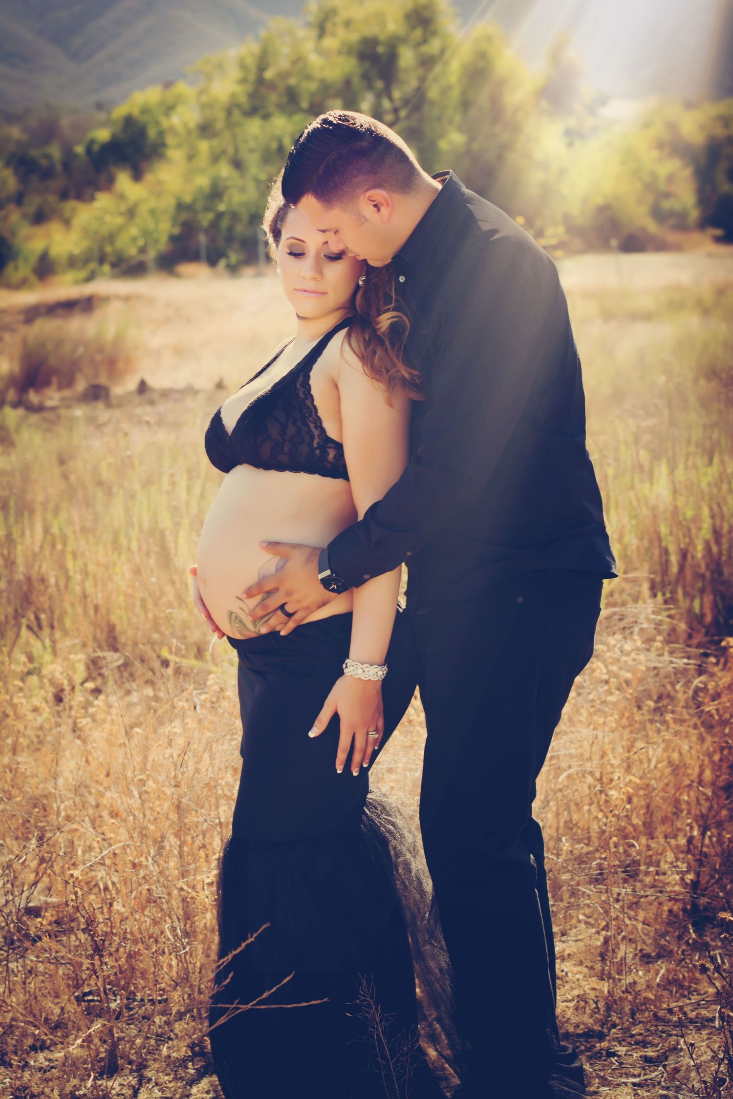 Intimate maternity photo of couple embracing in golden field at sunset.