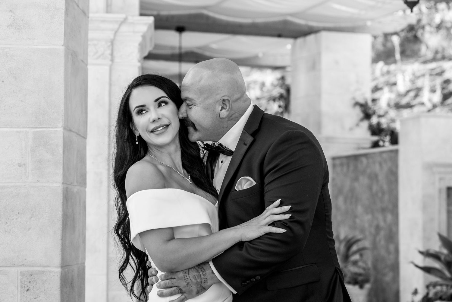 A black and white photo captures an intimate wedding moment between a couple sharing an embrace at an elegant venue.