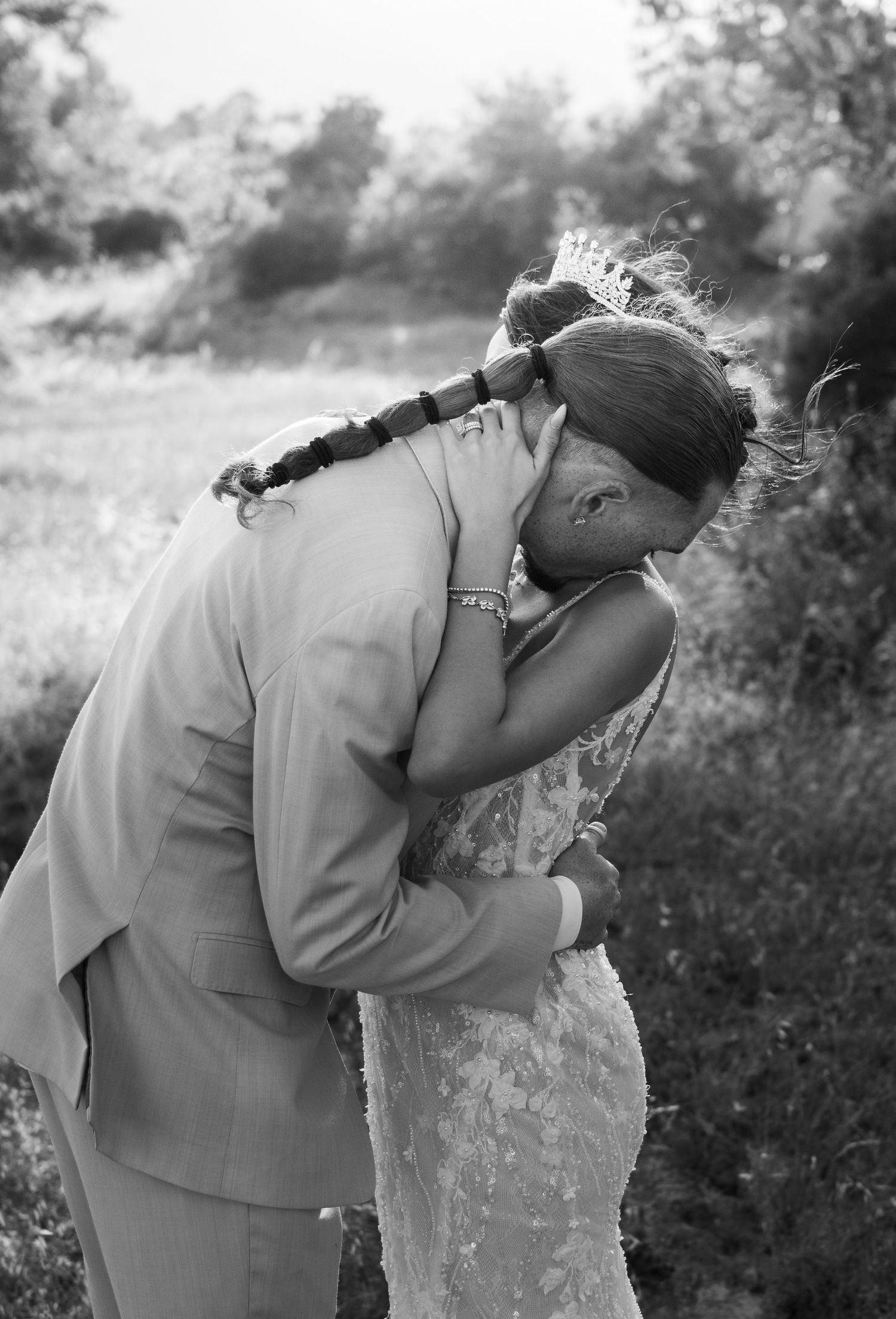 A romantic black and white wedding photography moment showing a couple embracing outdoors in a natural setting.