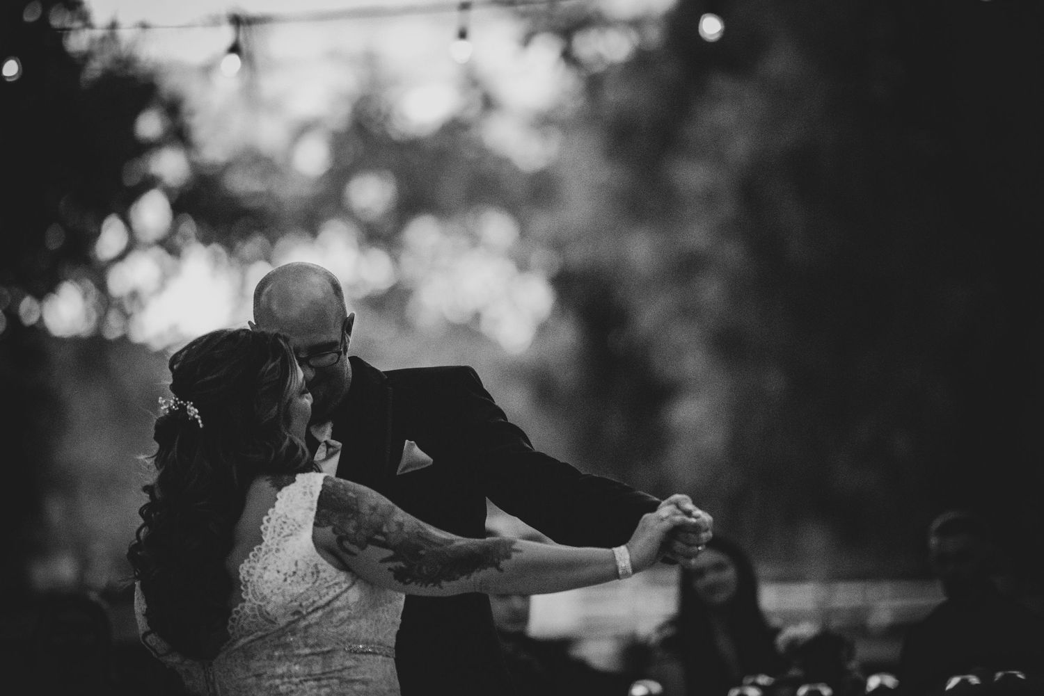 A black and white photo captures a romantic dancing moment between newlyweds in a dreamy outdoor setting.