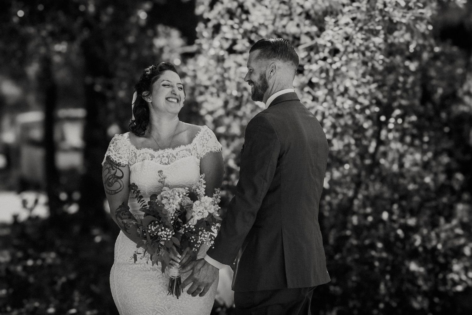 A joyful black and white wedding moment captured outdoors with blooming trees in the background.