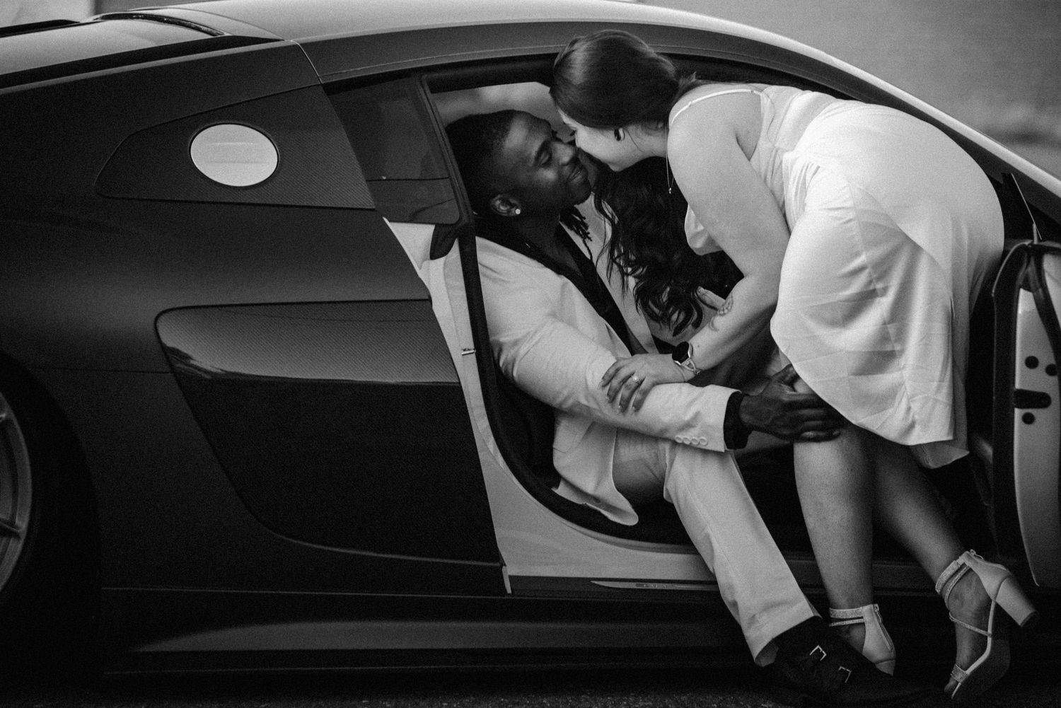 Black and white shot showing a romantic moment between two people by a car door.
