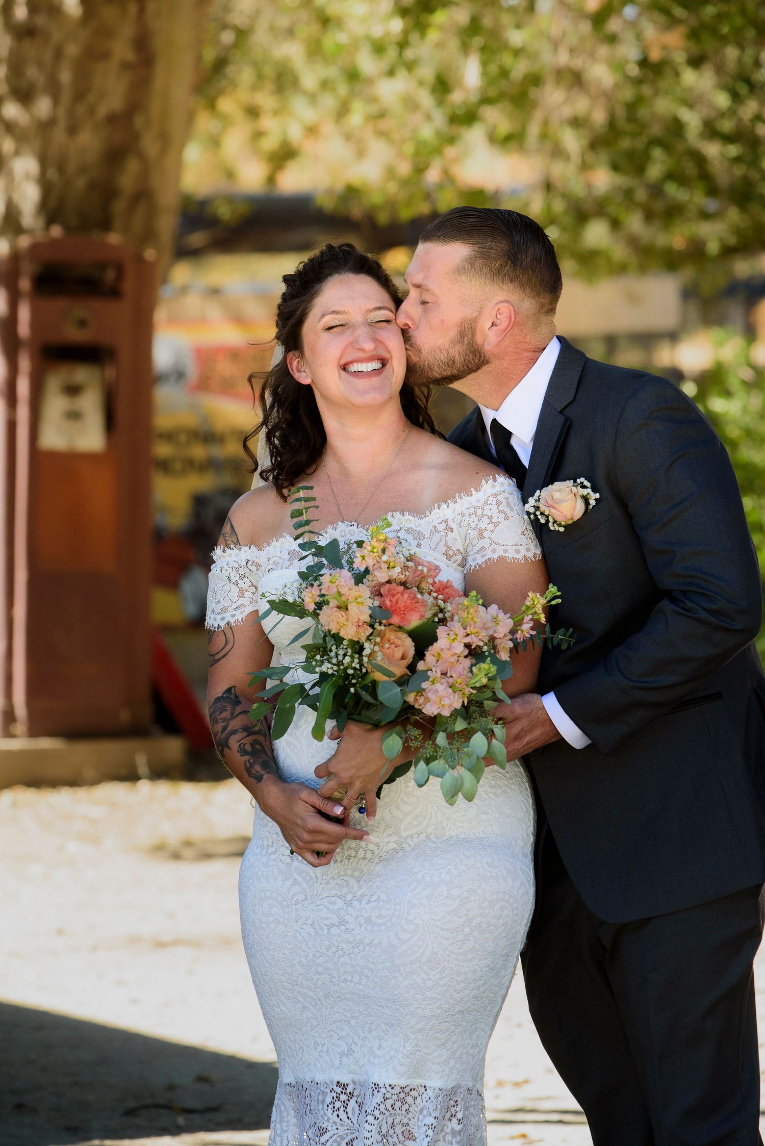 A joyful candid wedding moment outdoors with a lace dress, beautiful bouquet of peach and coral flowers, and a loving embrace.