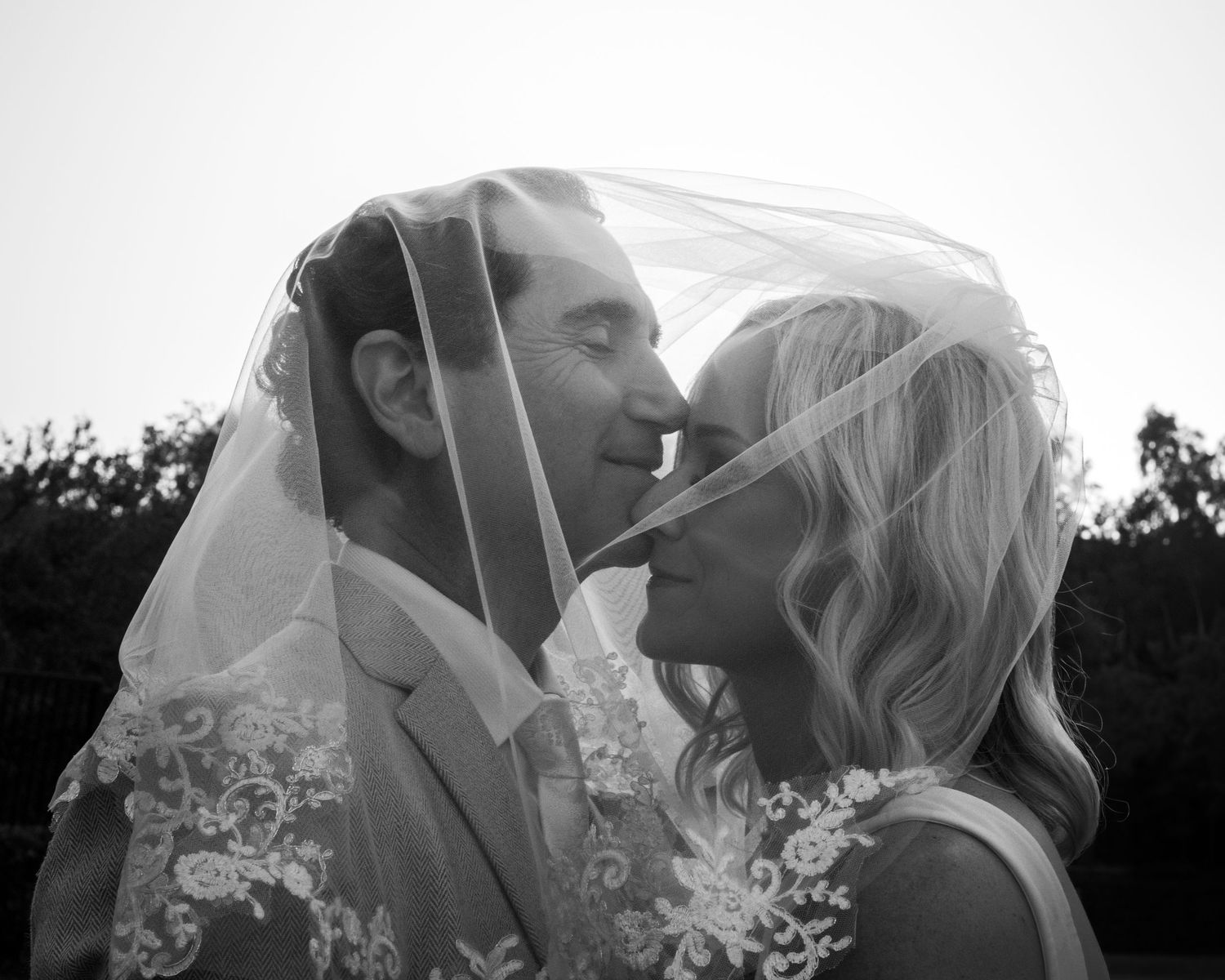 Black and white wedding photo of bride and groom sharing intimate moment under lace veil.