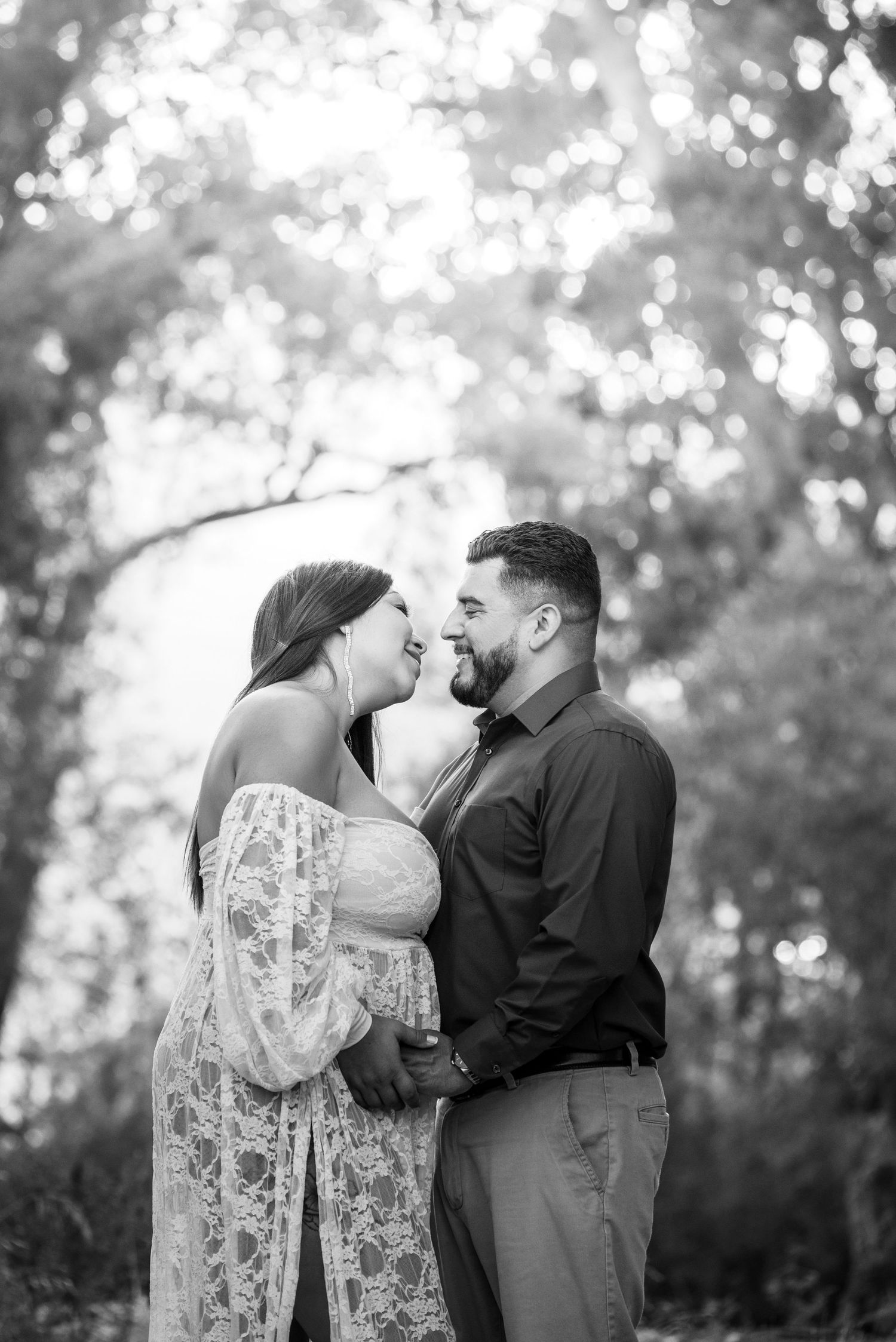 A romantic black and white portrait of a couple embracing outdoors with dreamy bokeh lighting in the background.